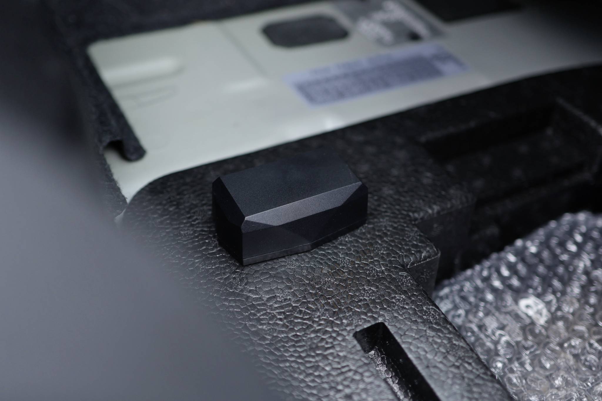 A black, faceted stone or object lies on a padded surface in an interior space.