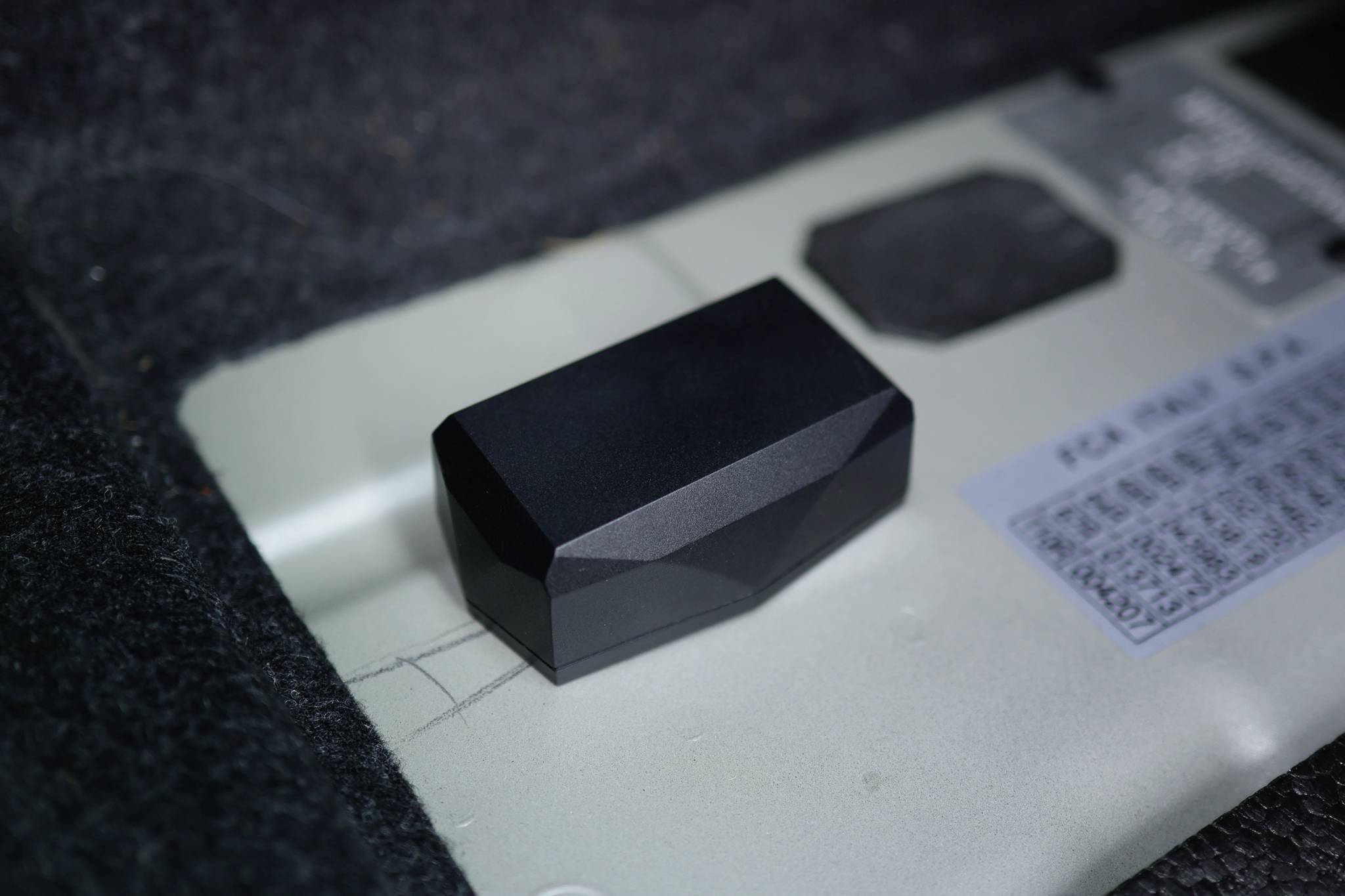 A black, faceted object lies on a grey surface, next to a sign with barely legible text and numbers.