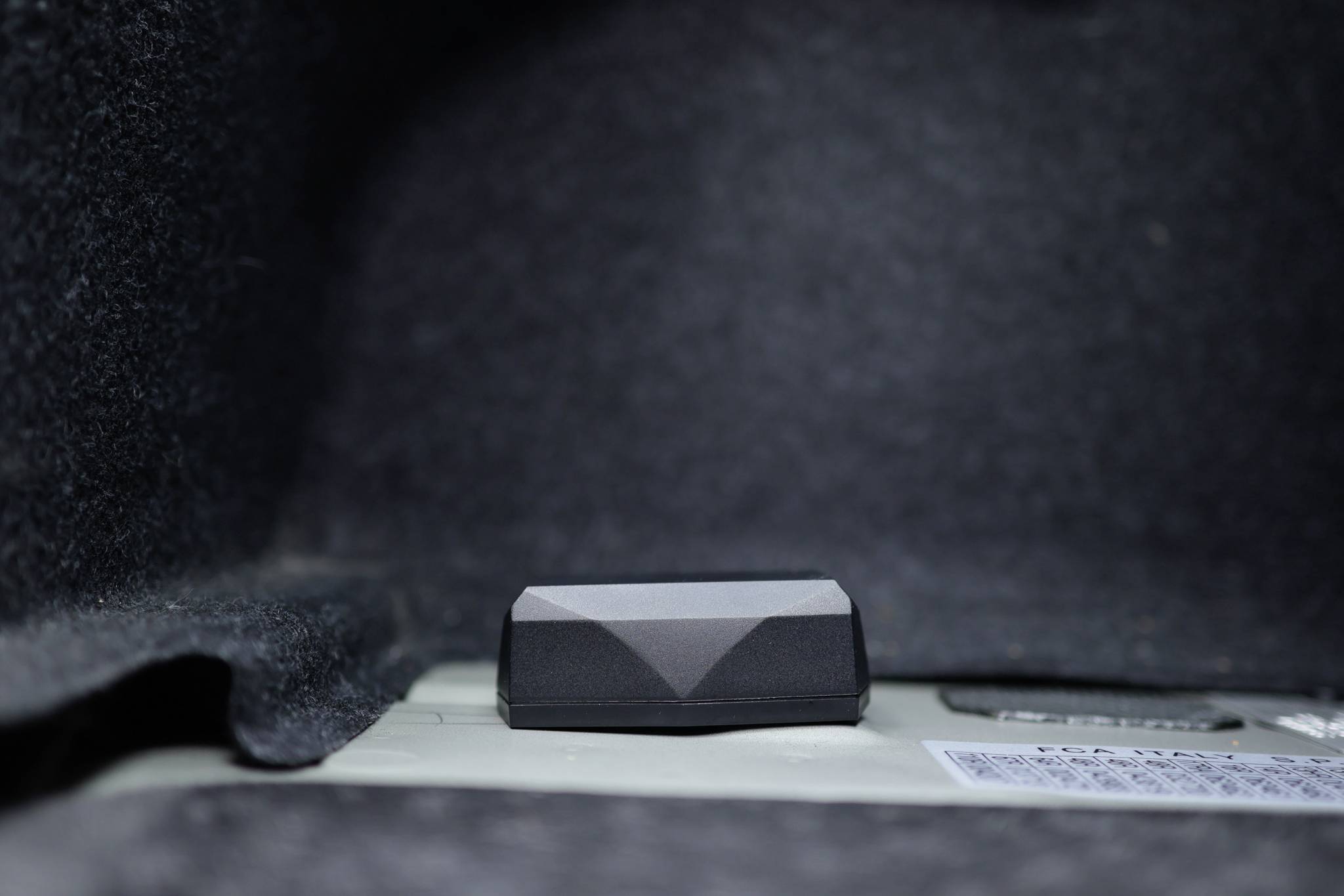 A black button in a grey, padded interior, possibly mounted in the boot of a car.