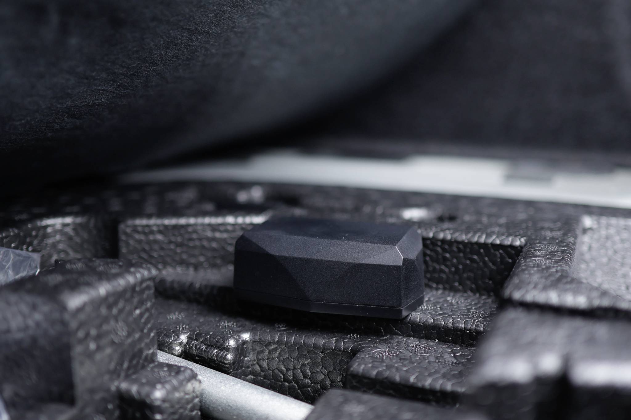 A black, faceted object lies in a precisely fitting foam recess within a case, surrounded by protective materials.