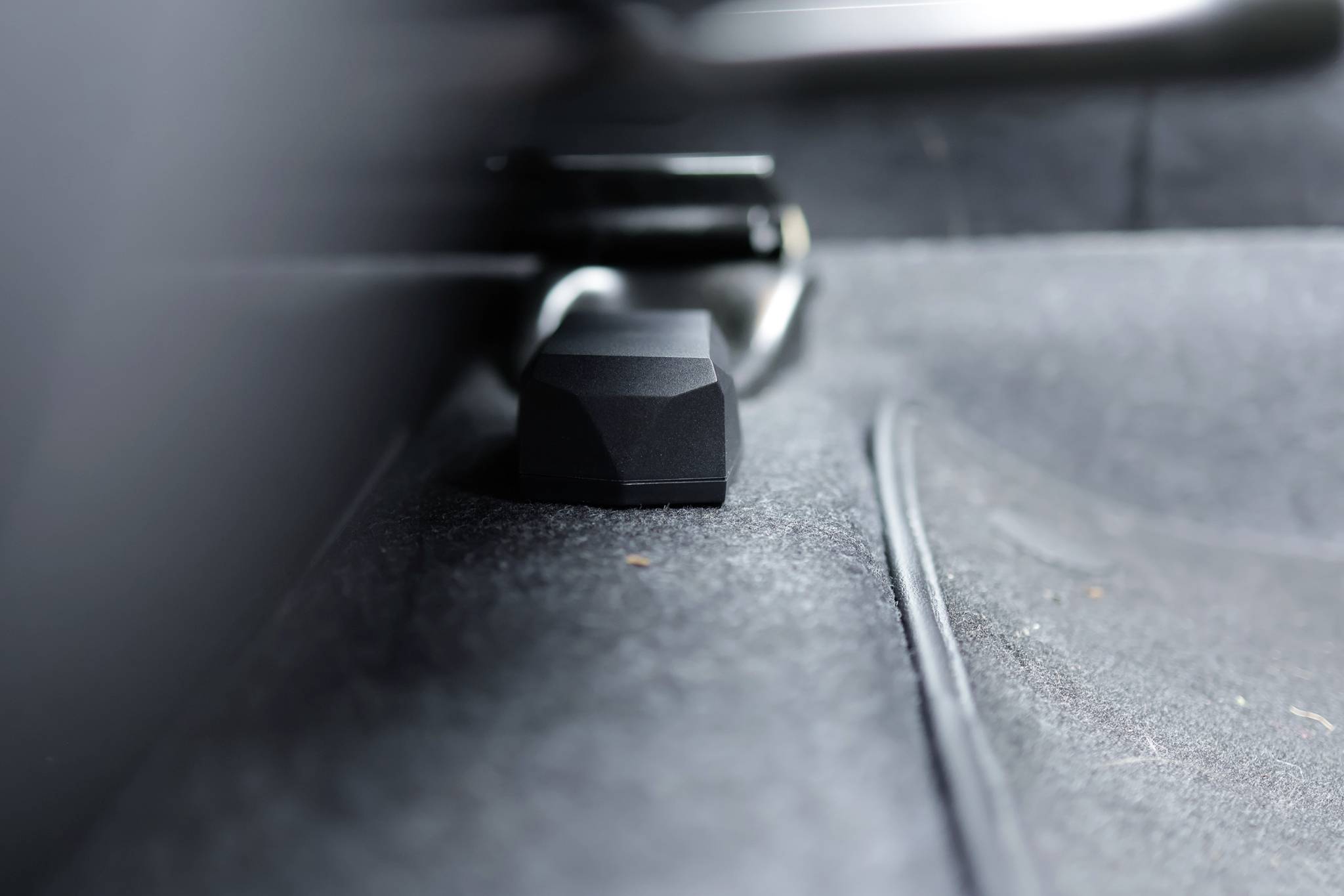 A black plastic block lies on a grey carpet. The block is centrally positioned in the image and enclosed by a metal frame.