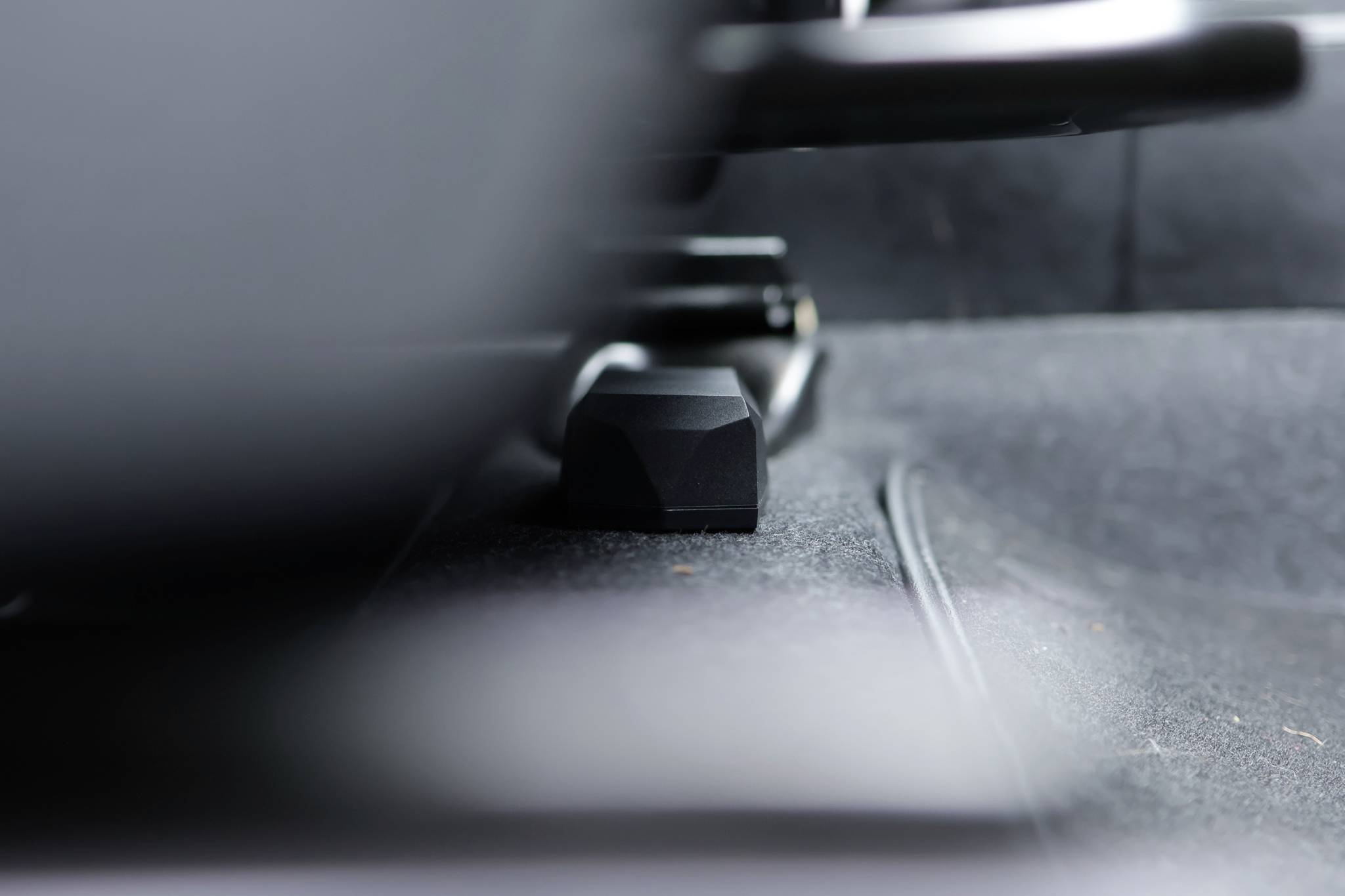 Beneath a car seat, a black plastic component is visible, which could potentially be an adjustment lever or fastening element. Background blurred.