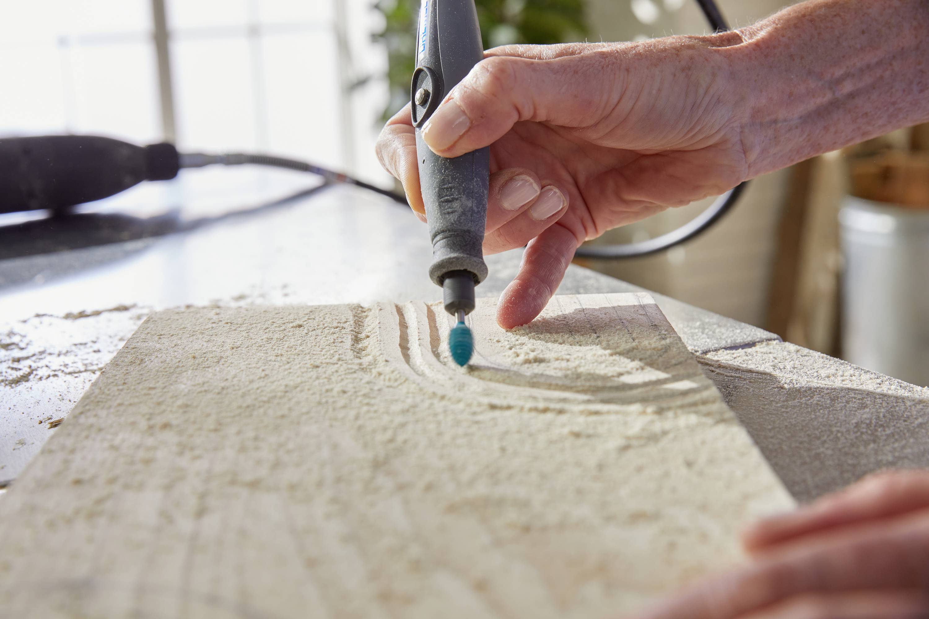 A hand guides an electric tool over a wooden board, carving a pattern into the surface.
