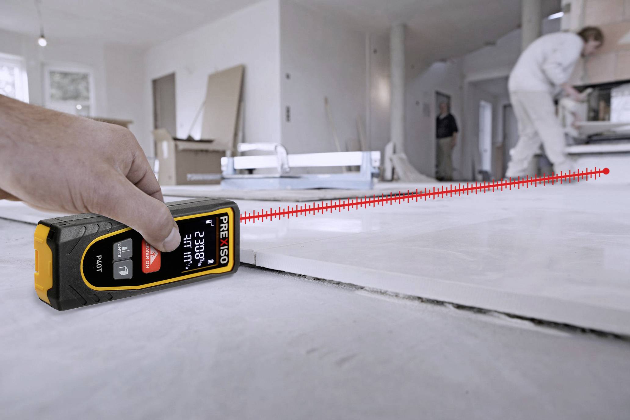 A hand is using a laser distance metre to measure the distance in a room, with construction work taking place in the background.