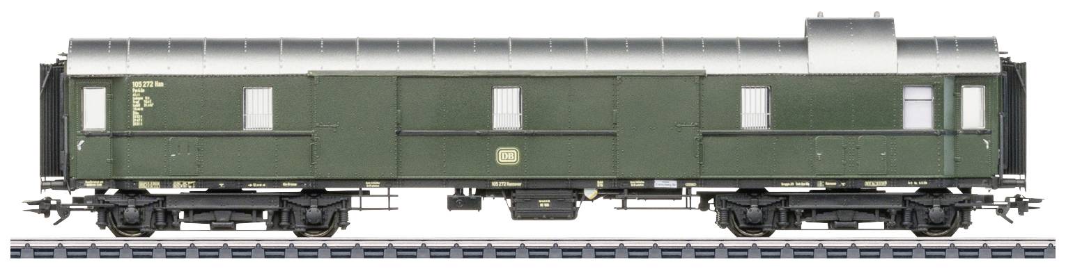 A green goods wagon with a silver roof stands on a railway track. The wagon has multiple doors and windows along its sides.