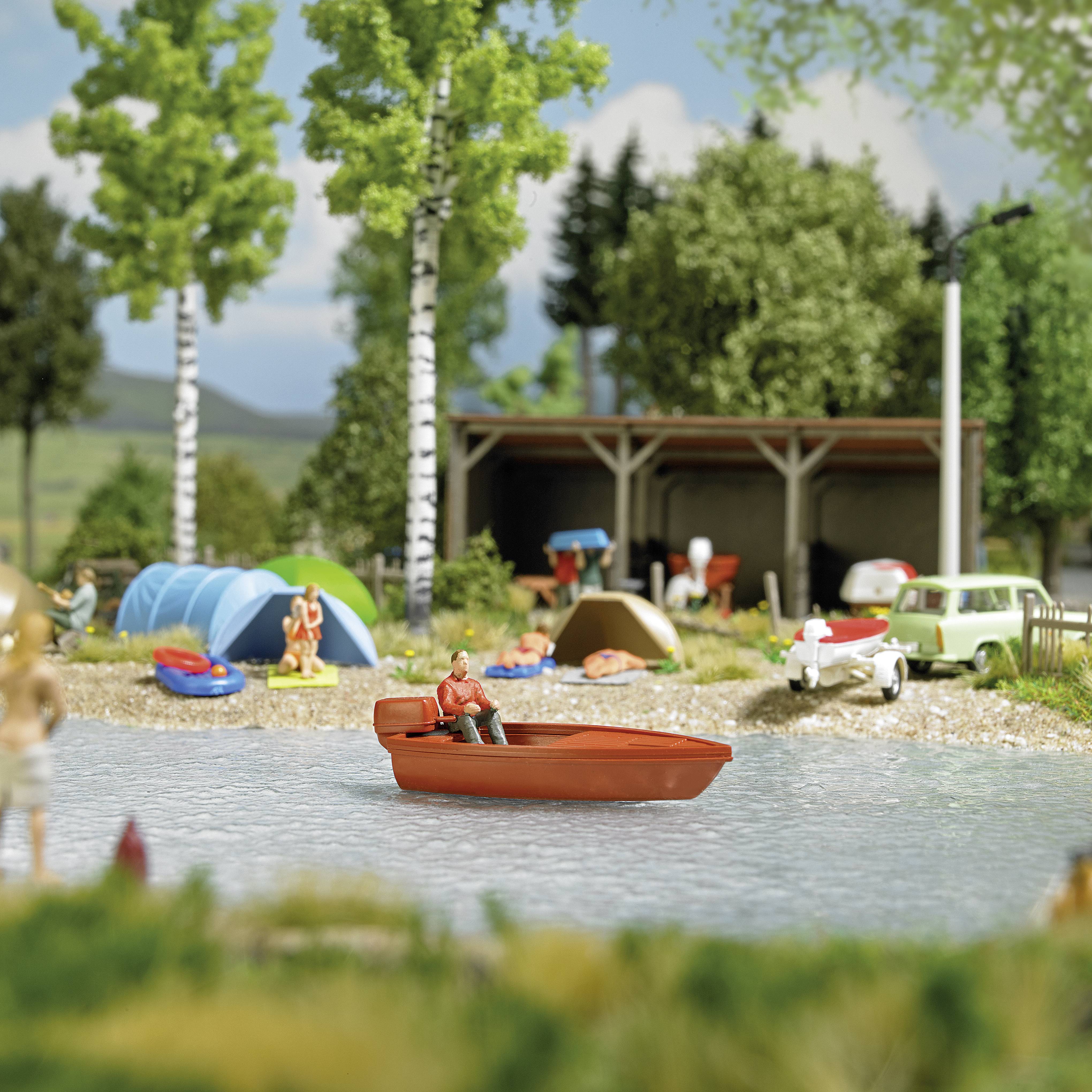 A man is fishing from a small boat on a pond. In the background, a campsite with tents, cars, and trees can be seen.