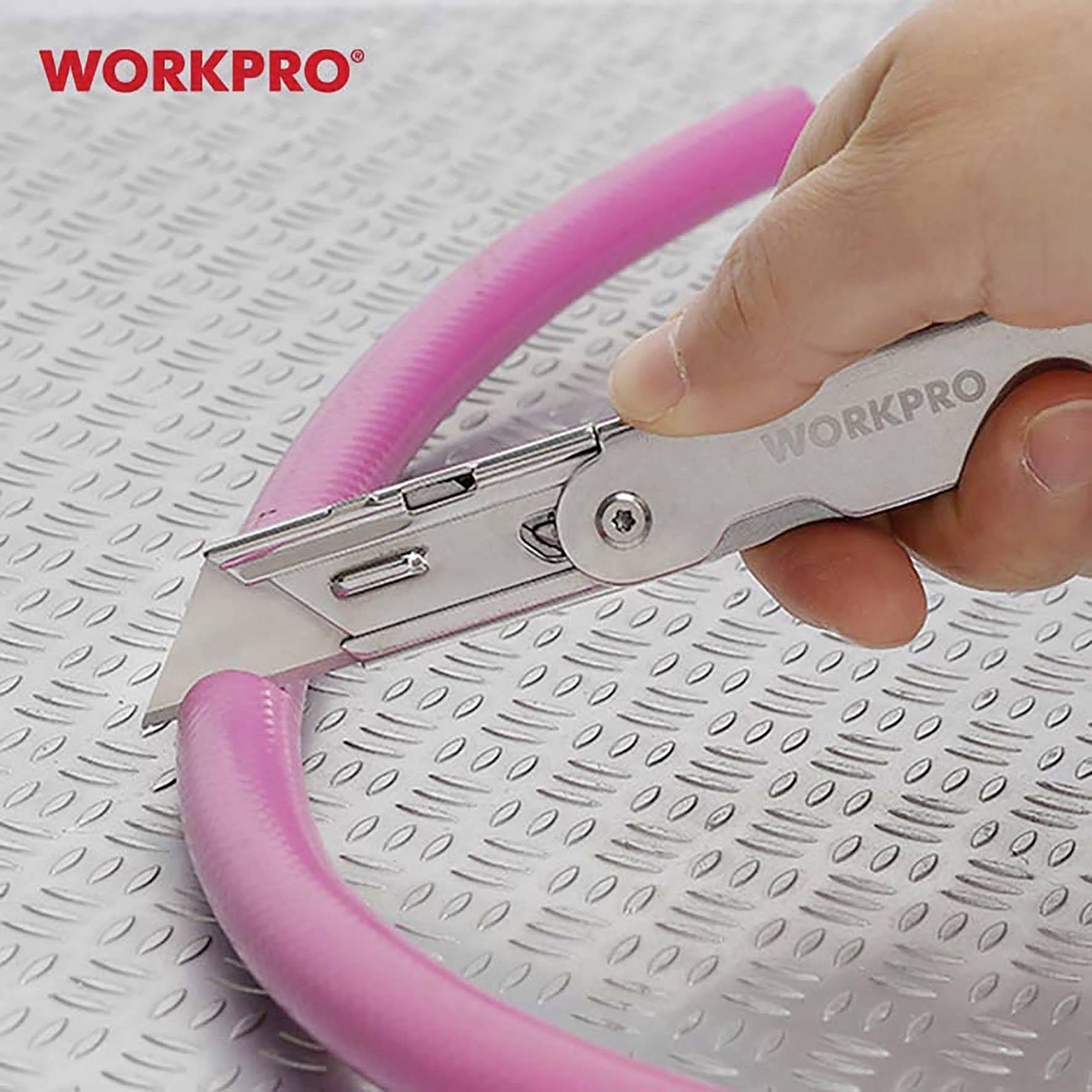 A hand is holding a silver WORKPRO universal knife, cutting a pink foam tube on a metallic, ridged surface.