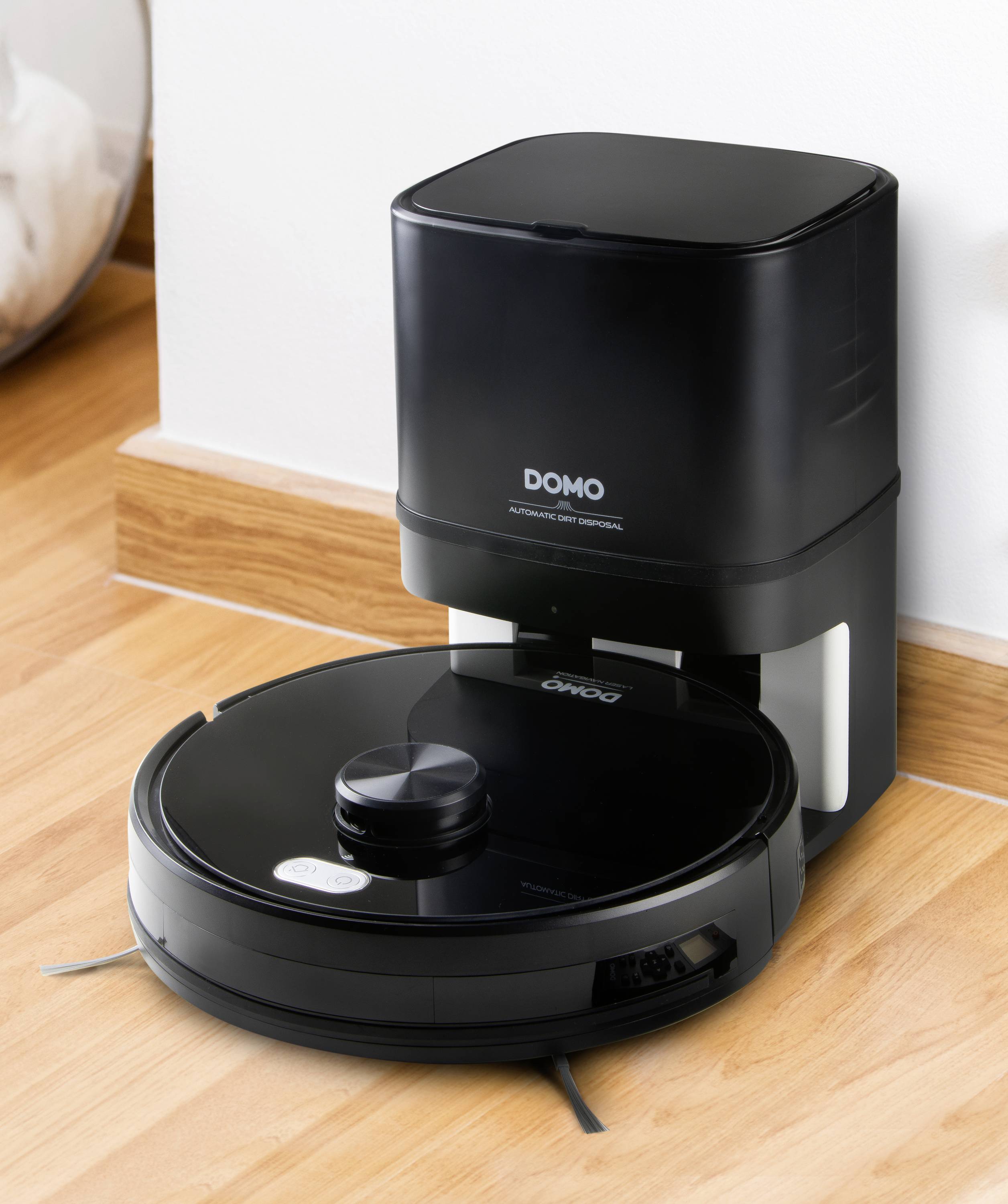 Robotic vacuum cleaner with a round shape and black glossy surface returns to its charging station. Wooden floor in the background.