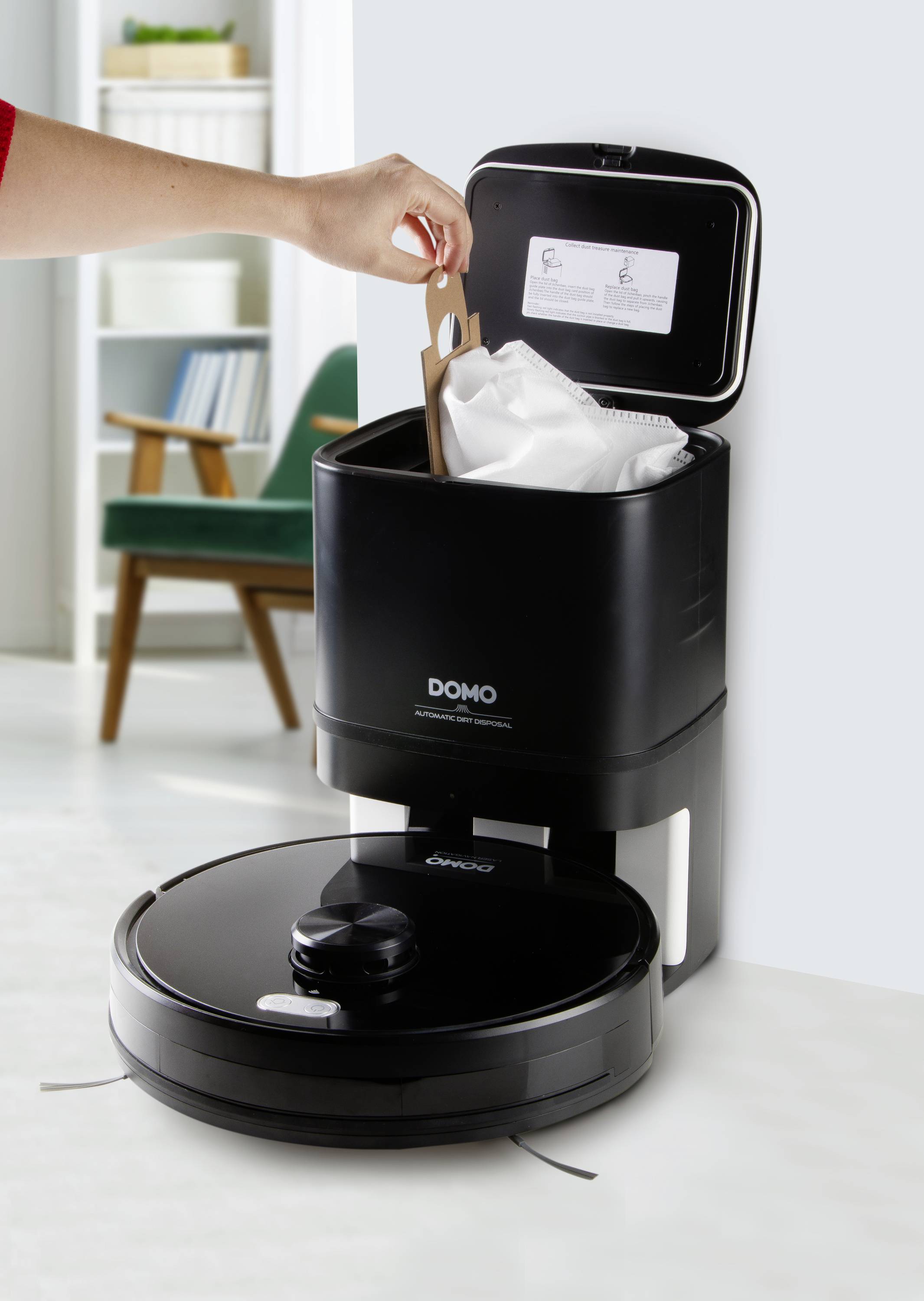 A person is emptying a robot vacuum into a docking station. The robot and station are black, with a bright living room in the background.