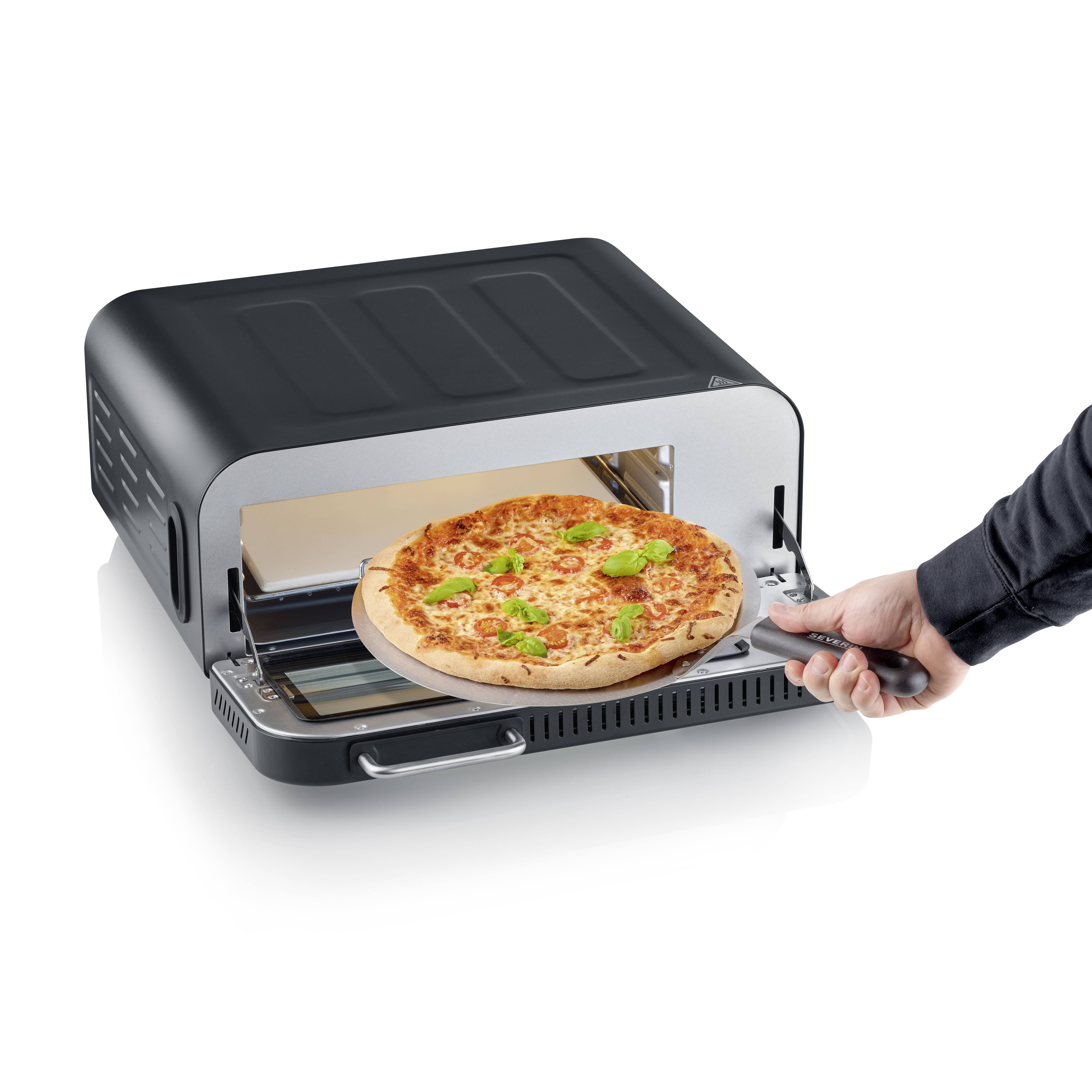 A pizza oven with an open door reveals a freshly baked pizza with melted cheese and green leaves on a pizza paddle.