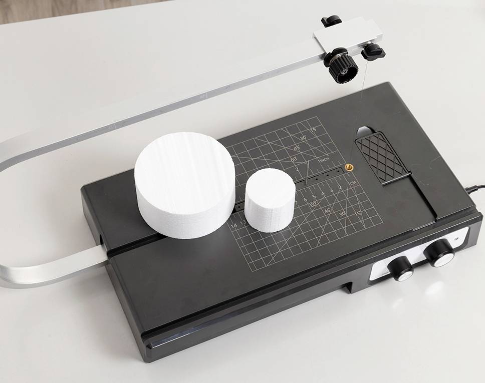 A black cutting plotter with two white, cylindrical objects of different sizes on the measuring table.