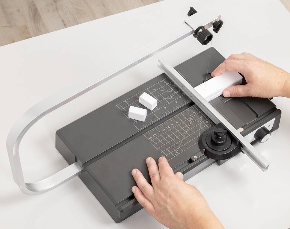 A person is cutting foam blocks using a cutting machine. Hands are holding and moving the material on the equipment.