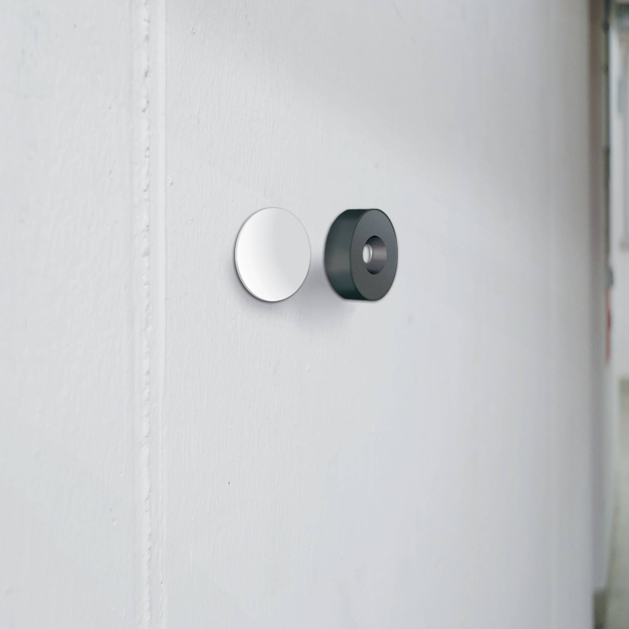Two round wall hooks, one silver, the other black, mounted on a white wall.