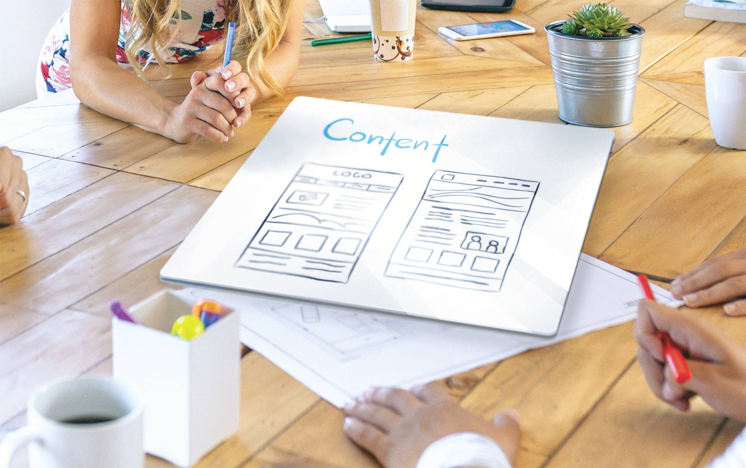 A group of people is planning a content strategy, discussing around a table with sketches of website layouts.