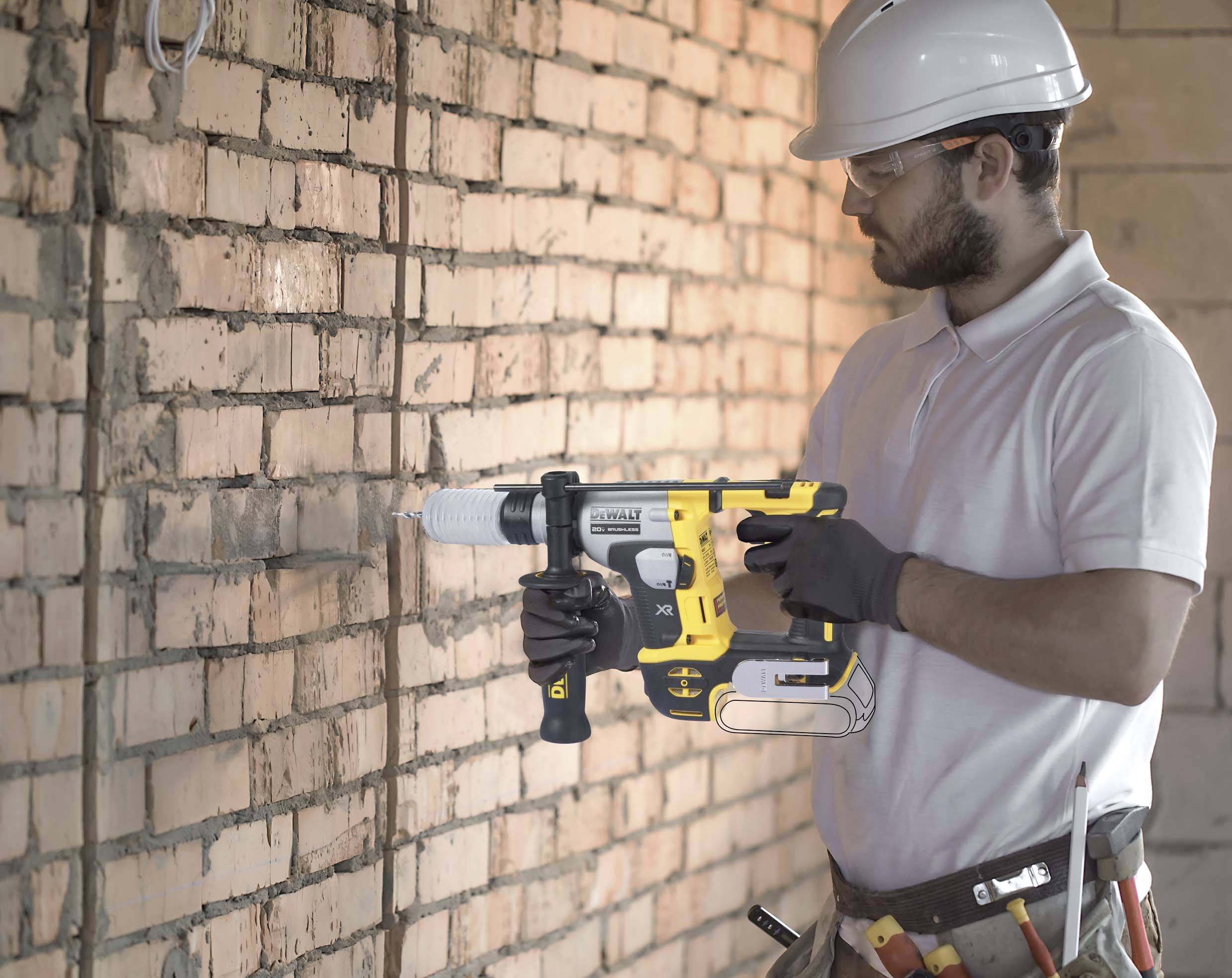 A construction worker wearing a hard hat and safety glasses is using a drill to bore into a brick wall.