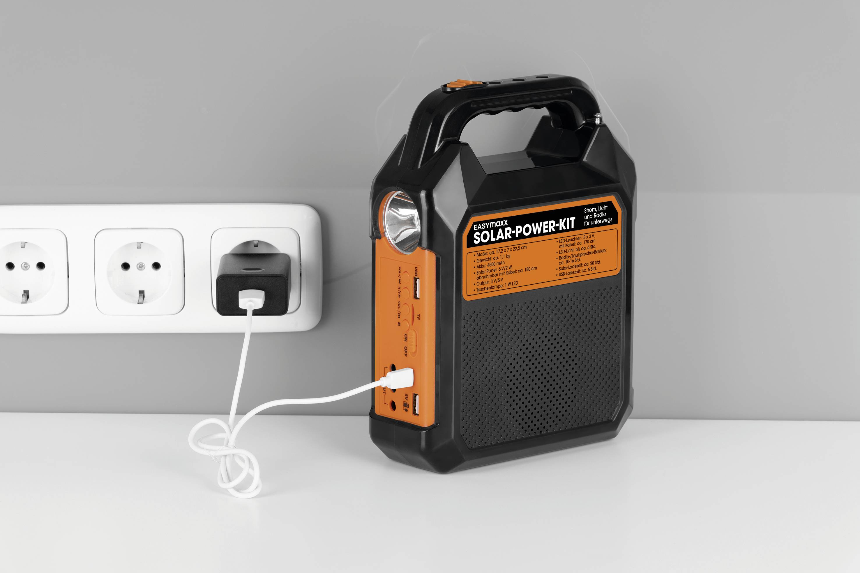 A portable, orange-black solar power unit is connected to a power socket. It has multiple device ports.