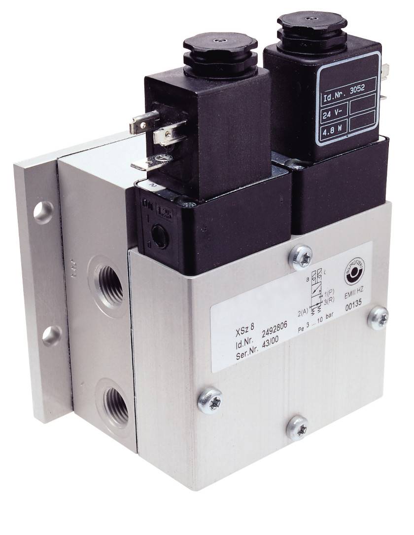 Solenoid valve with two electromagnetic coils, metal base and label with technical specifications.