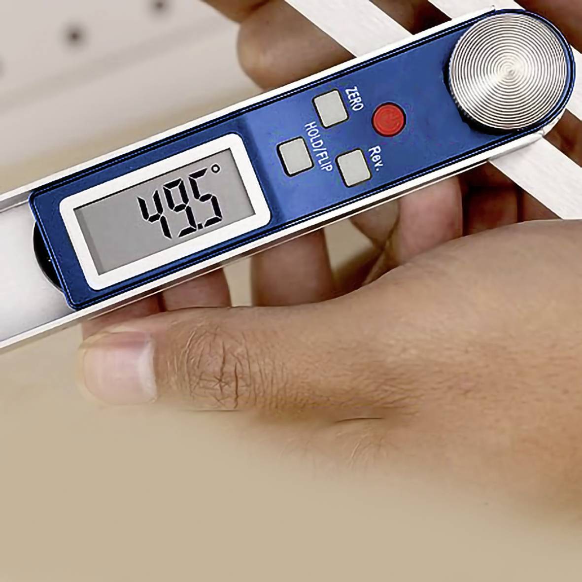 A hand is holding a digital protractor displaying an angle of 49.5 degrees on its screen. Device buttons are visible.