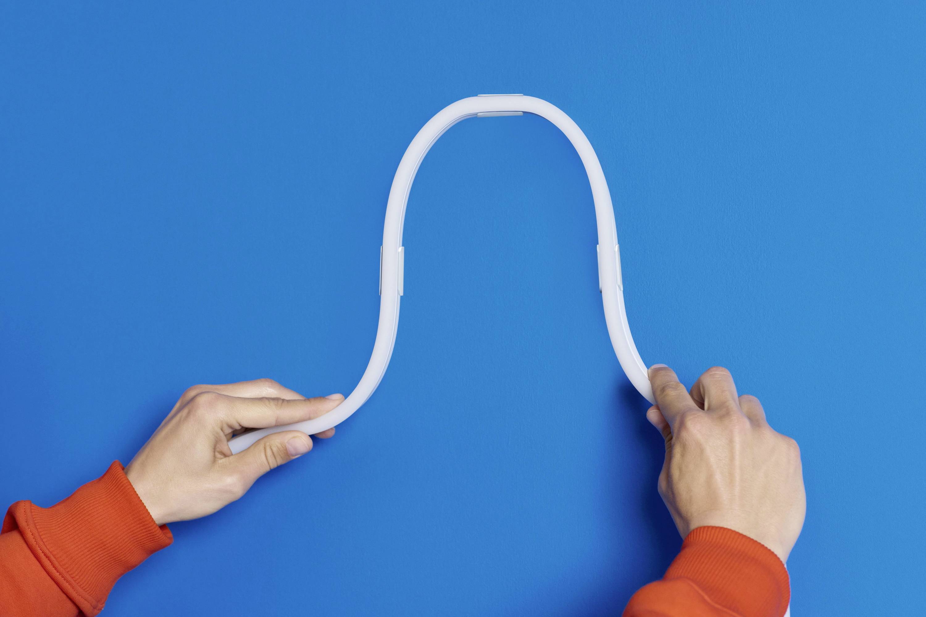 Two hands in red sleeves bend a white, flexible pipe into the shape of an inverted 'U' against a blue background.