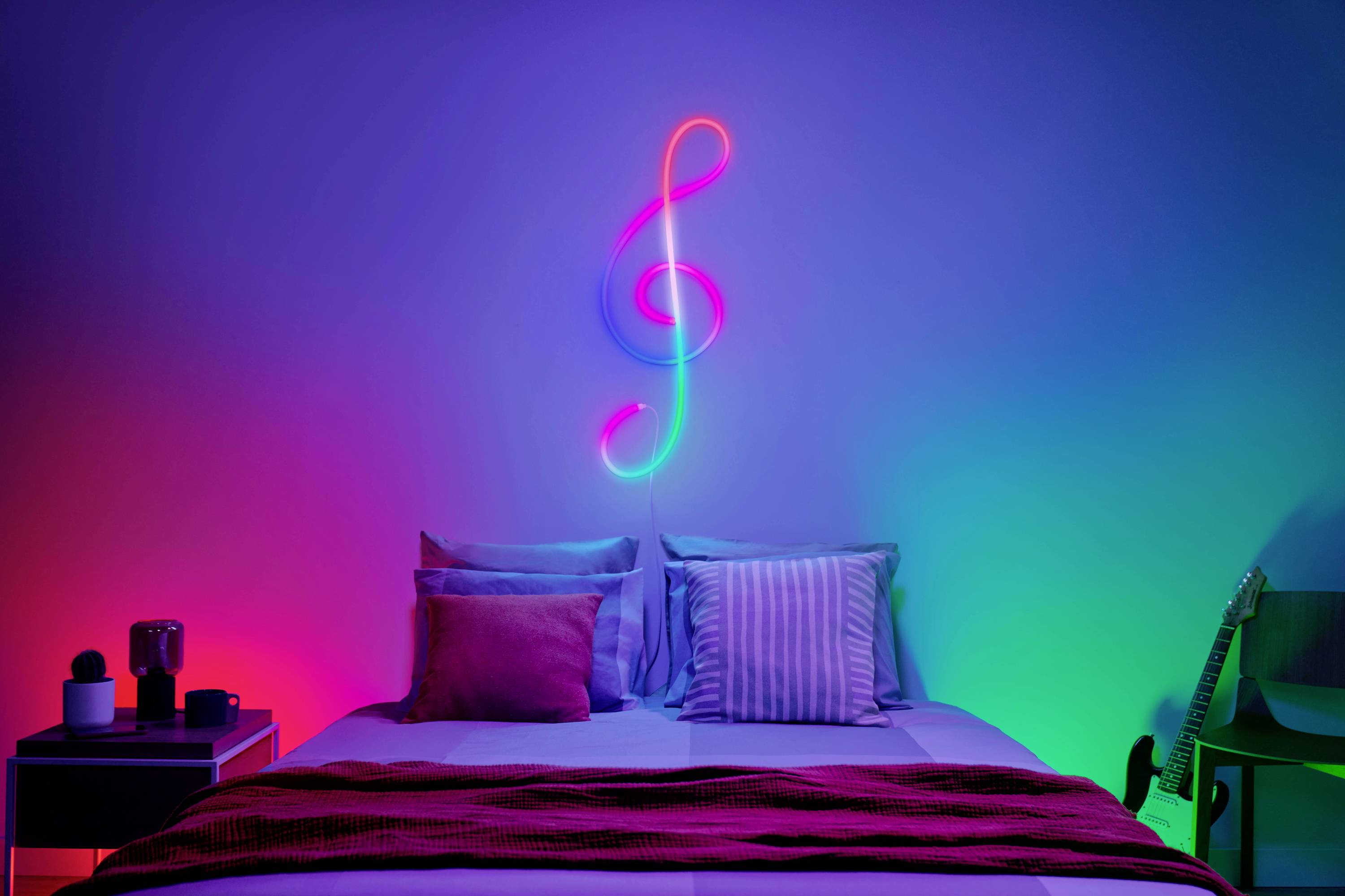 A neon-coloured treble clef on the wall above a bed with colourful cushions, atmospheric lighting in blue, red and green.