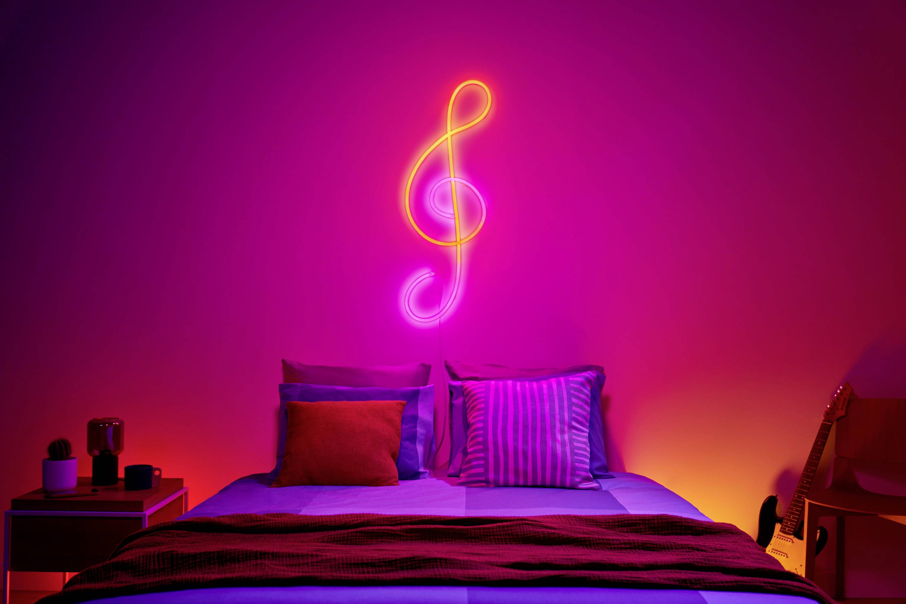 Bedroom with an illuminated treble clef on the wall, colourful cushions on the bed, and a guitar in the corner.