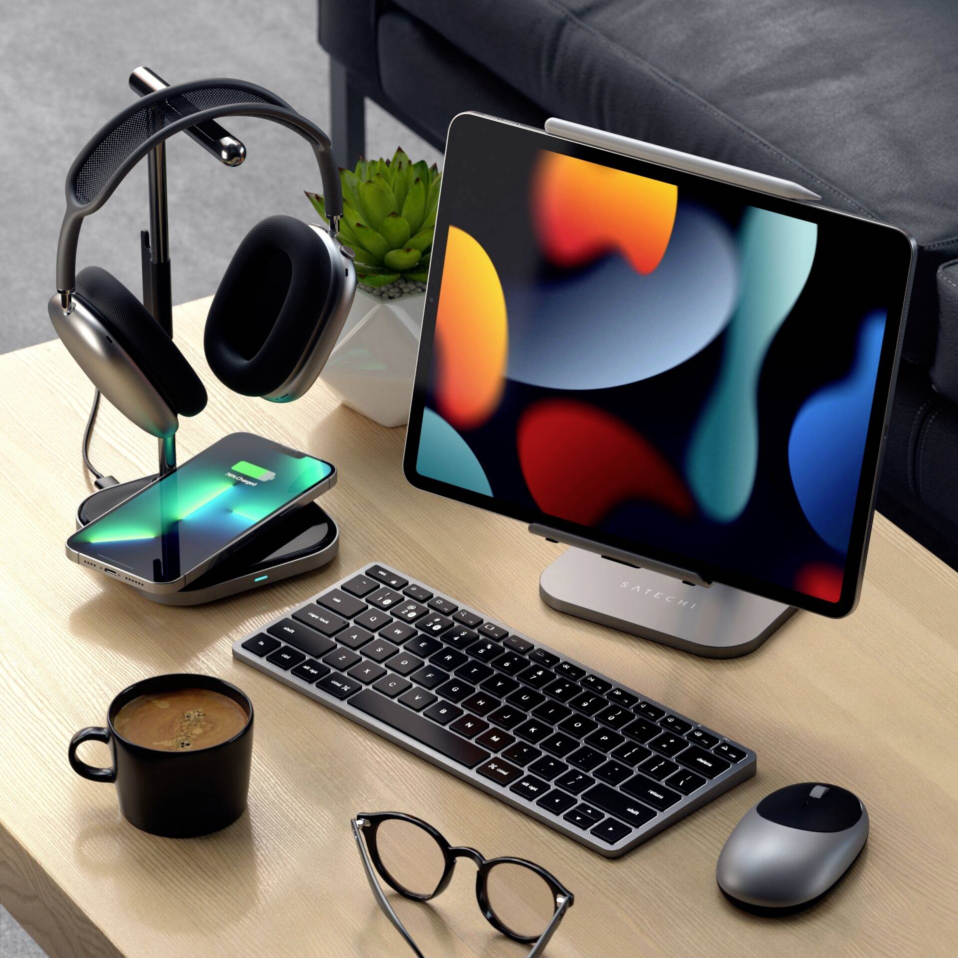 A tidy desk with a tablet on a stand, wireless keyboard, mouse, headphones and a cup of coffee, with a pair of glasses nearby.