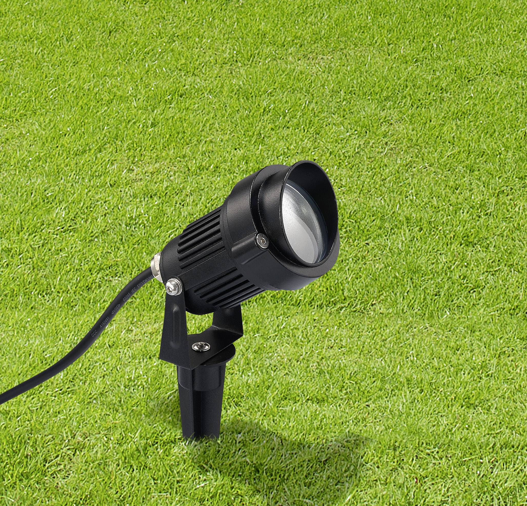 A black landscape spotlight is mounted on a grassy lawn, aimed at an upward angle.