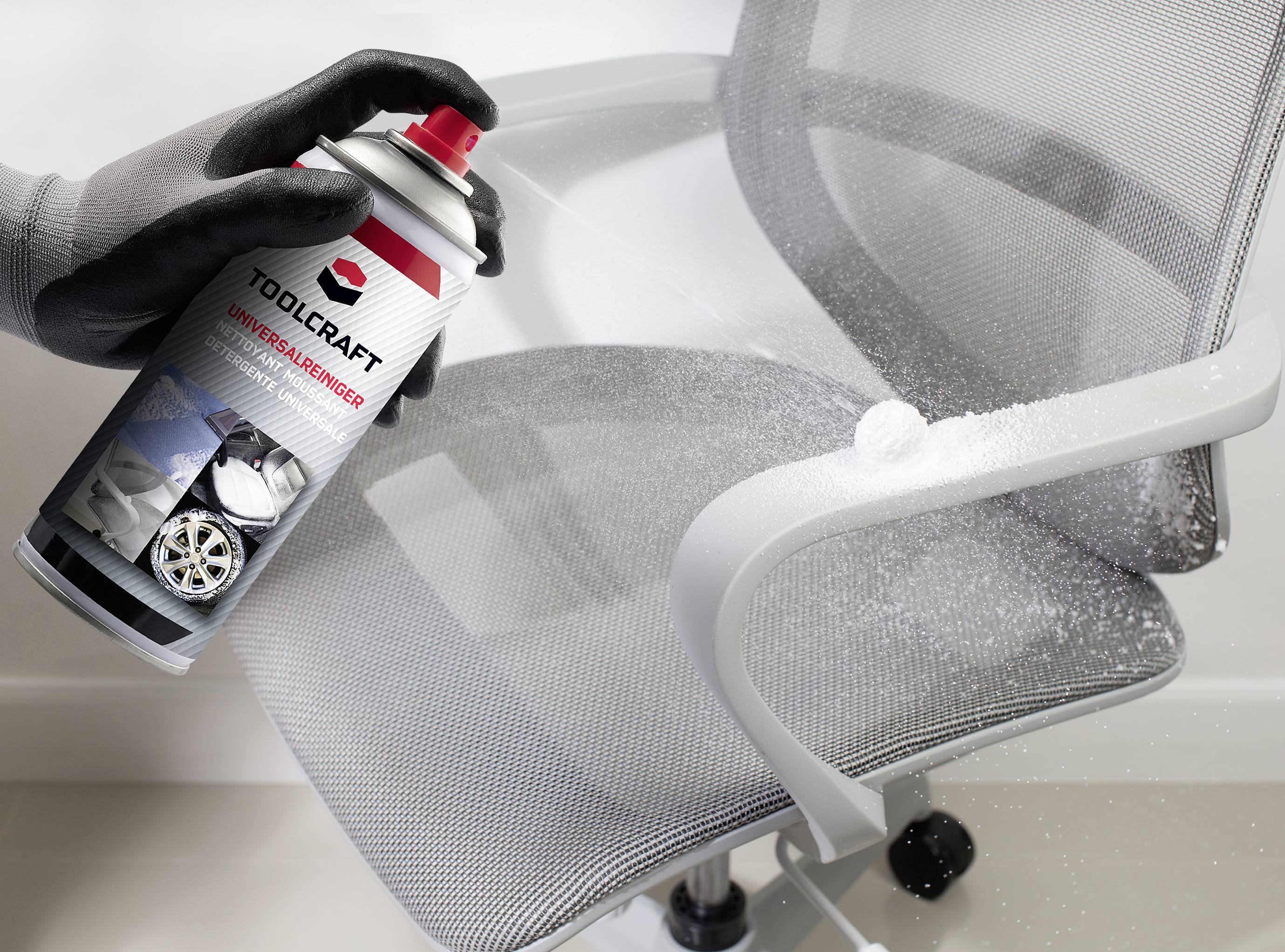 A hand is spraying a de-icing agent onto a metallic office chair, most likely for cleaning or removing adhesive residue.