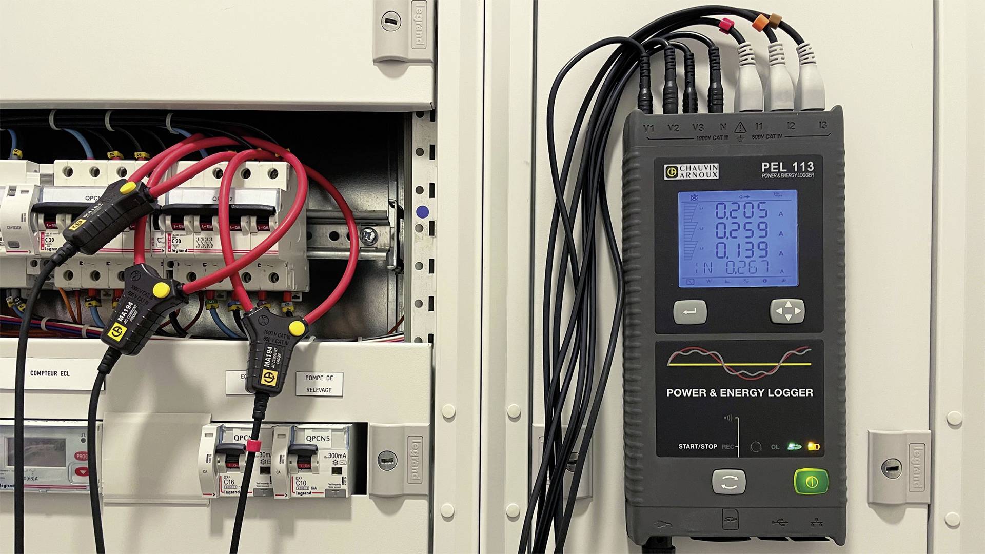 An energy logger measures electrical values in an electrical cabinet, displayed on the device screen with cable connections to the modules.