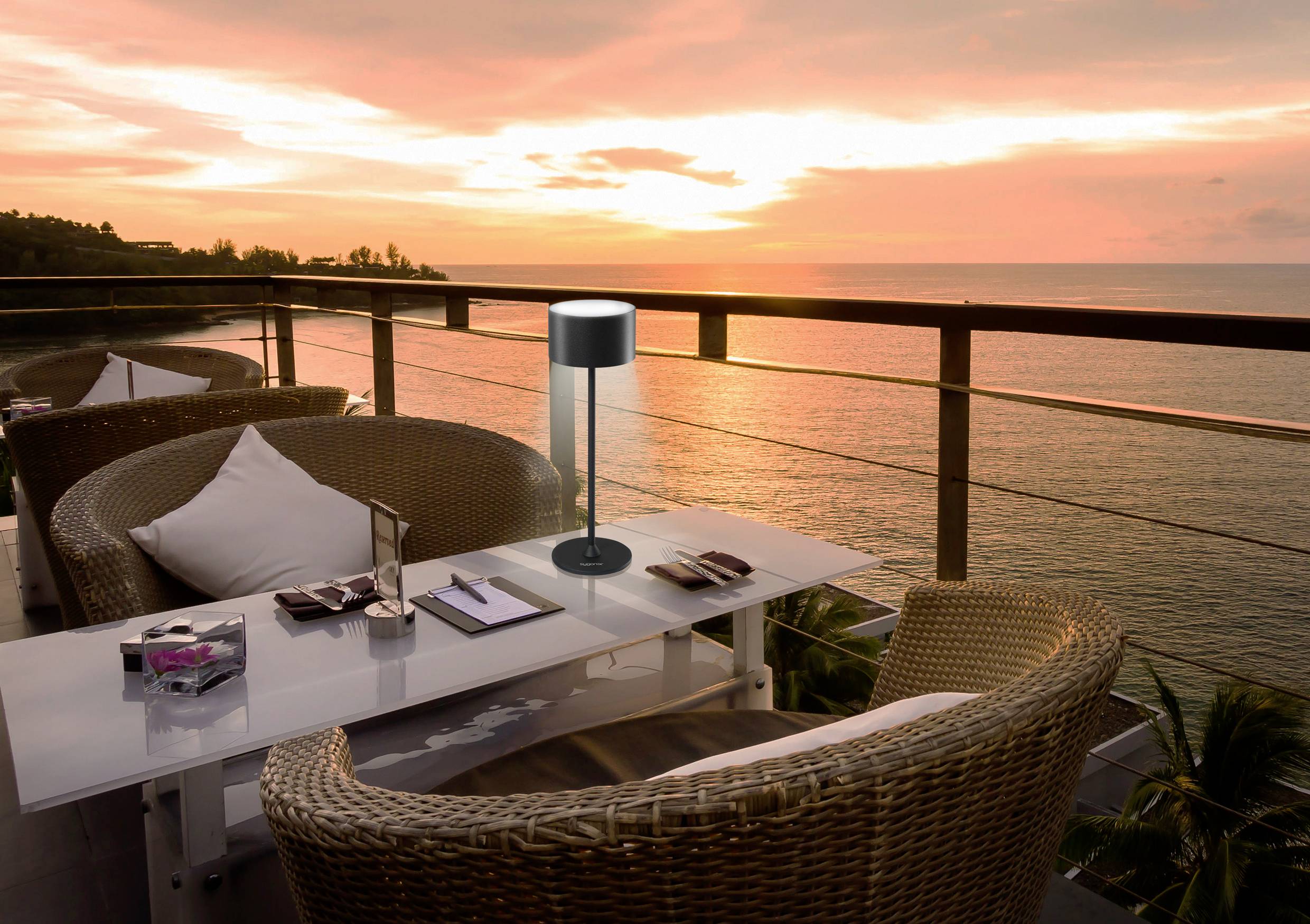 Sunset on a terrace with wicker chairs and a table. View of the sea with a warm, orange sky backdrop.