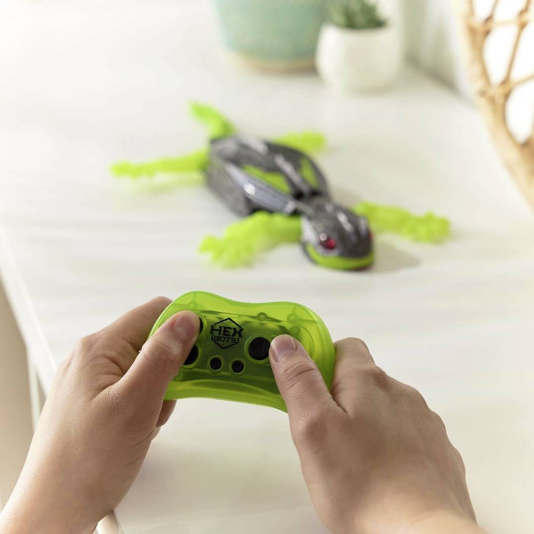 A person is controlling a green, mechanical toy animal on a table using a remote control.