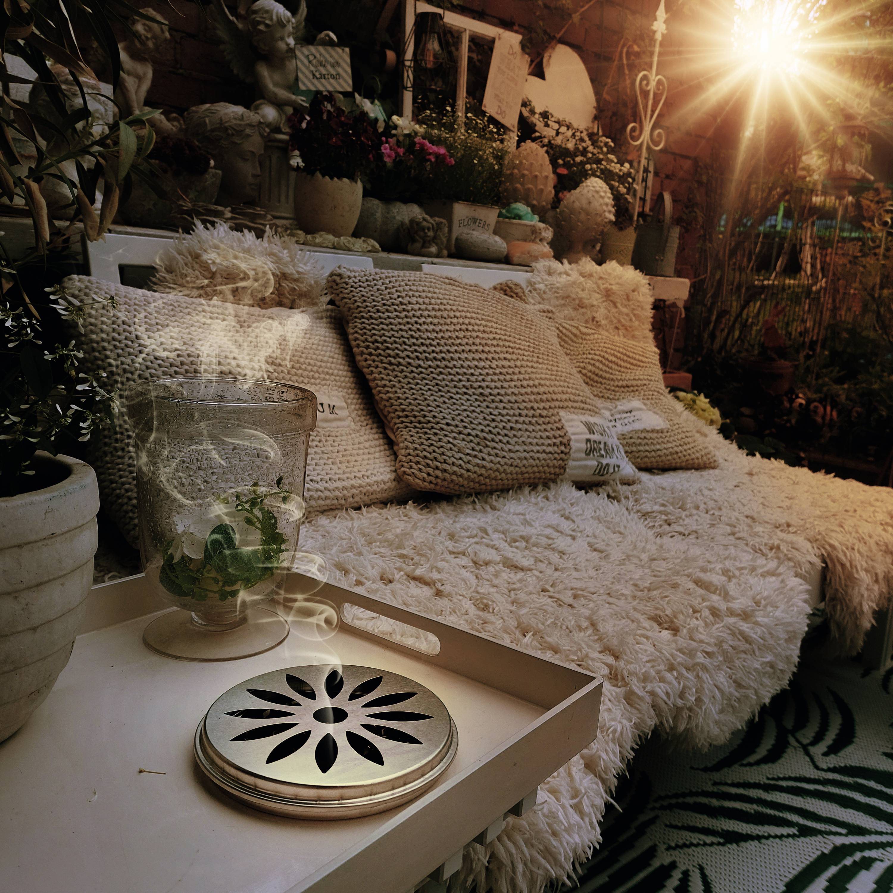 Cosy seating area with fluffy cushions and plants. Sunlight streams from above, creating a warm atmosphere.