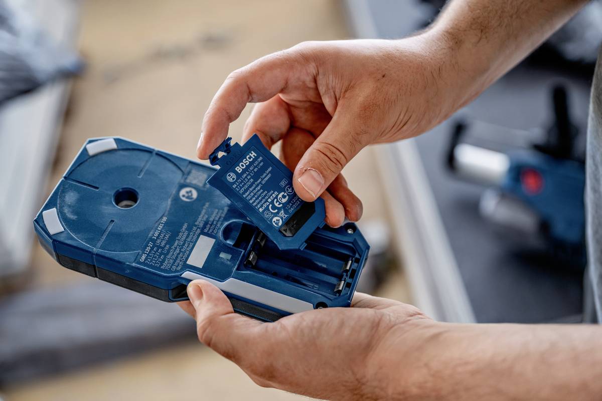A person is inserting a Bosch battery into an electronic device. The device and the battery are blue.