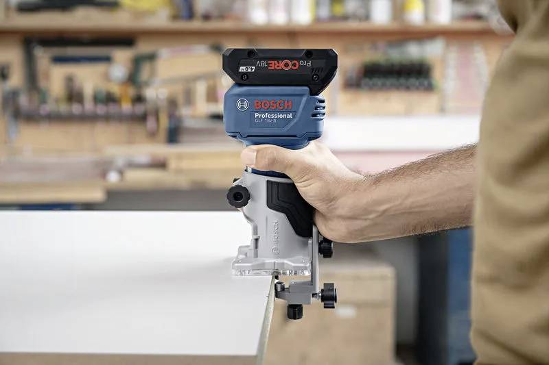 A person using a Bosch Professional router, holding it firmly against a piece of wood in a workshop setting, focused on precision woodworking.