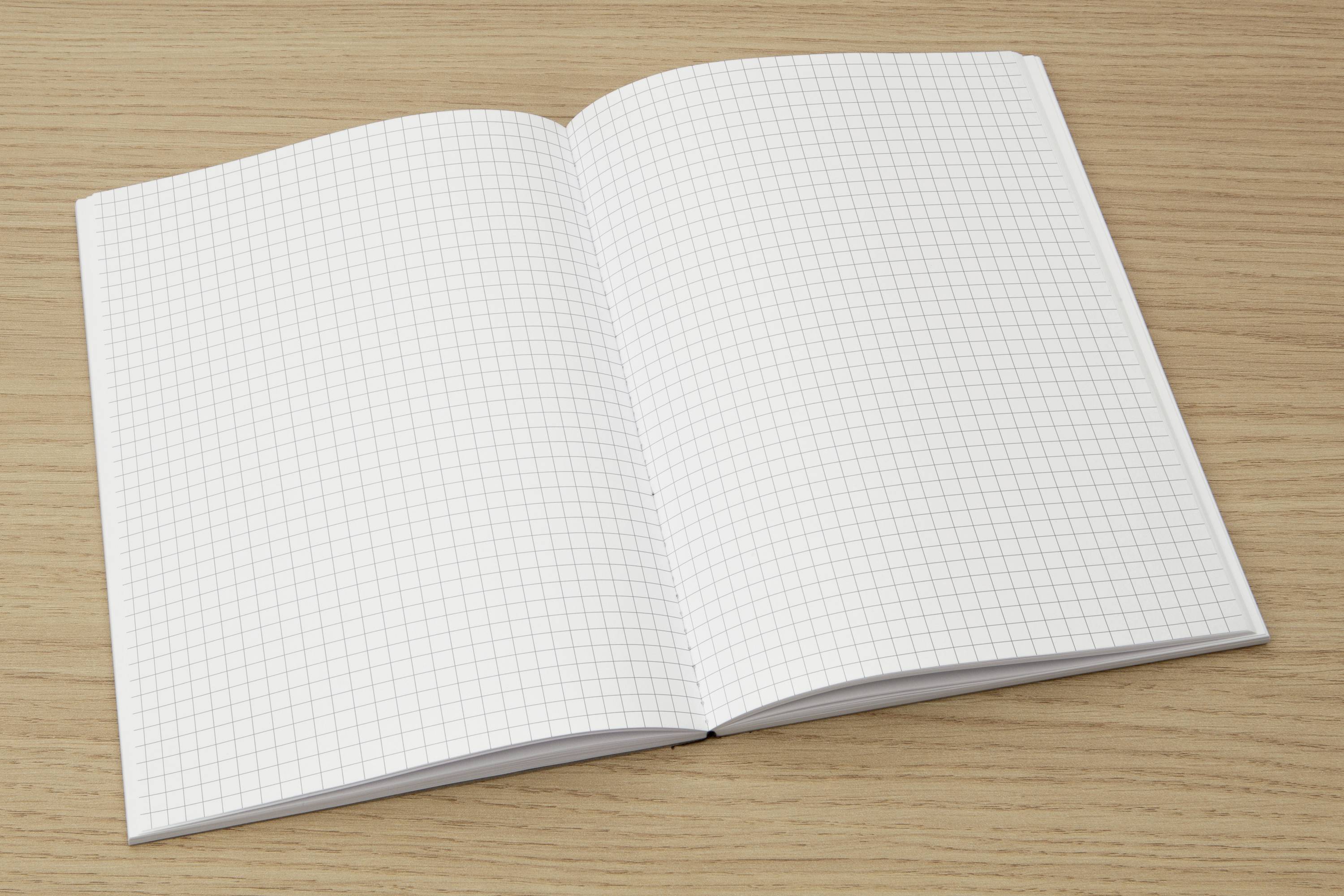 An open notebook with squared pages lies on a wooden table.