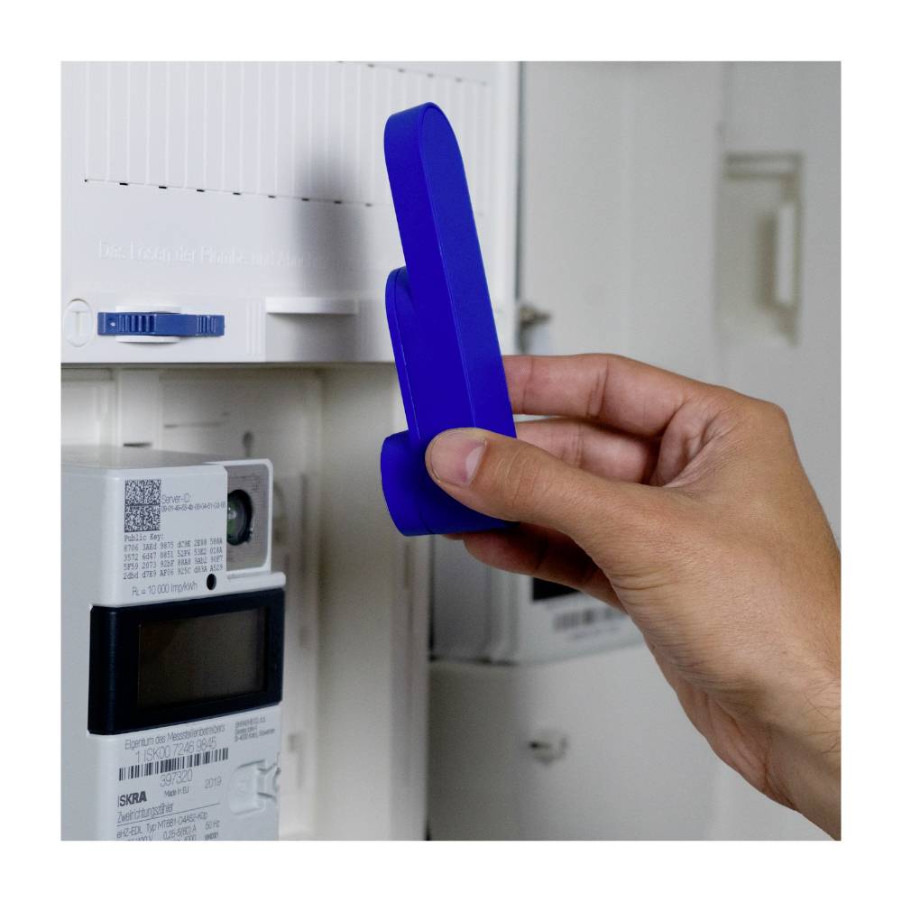 A hand is holding a blue device in front of a digital electricity metre, likely capturing data.