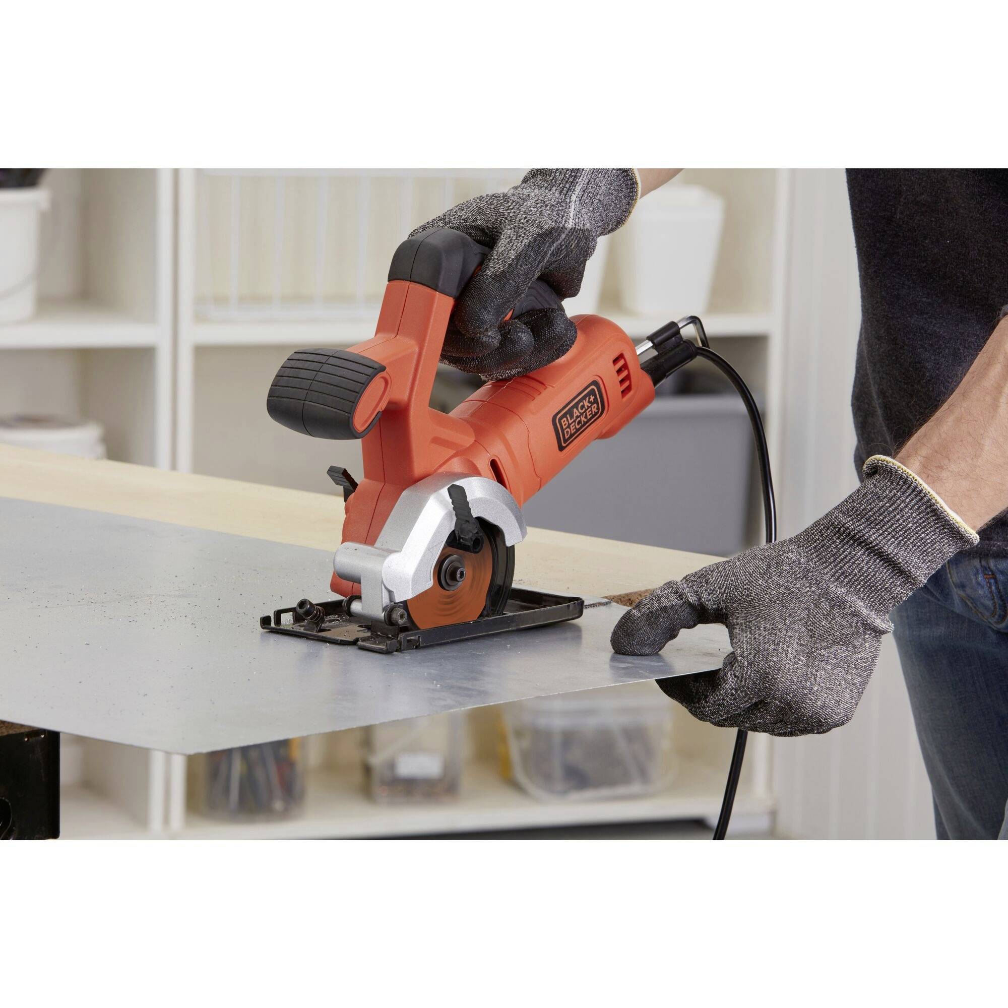 A person is cutting a piece of metal with a small, red circular saw. They are wearing work gloves for safety.