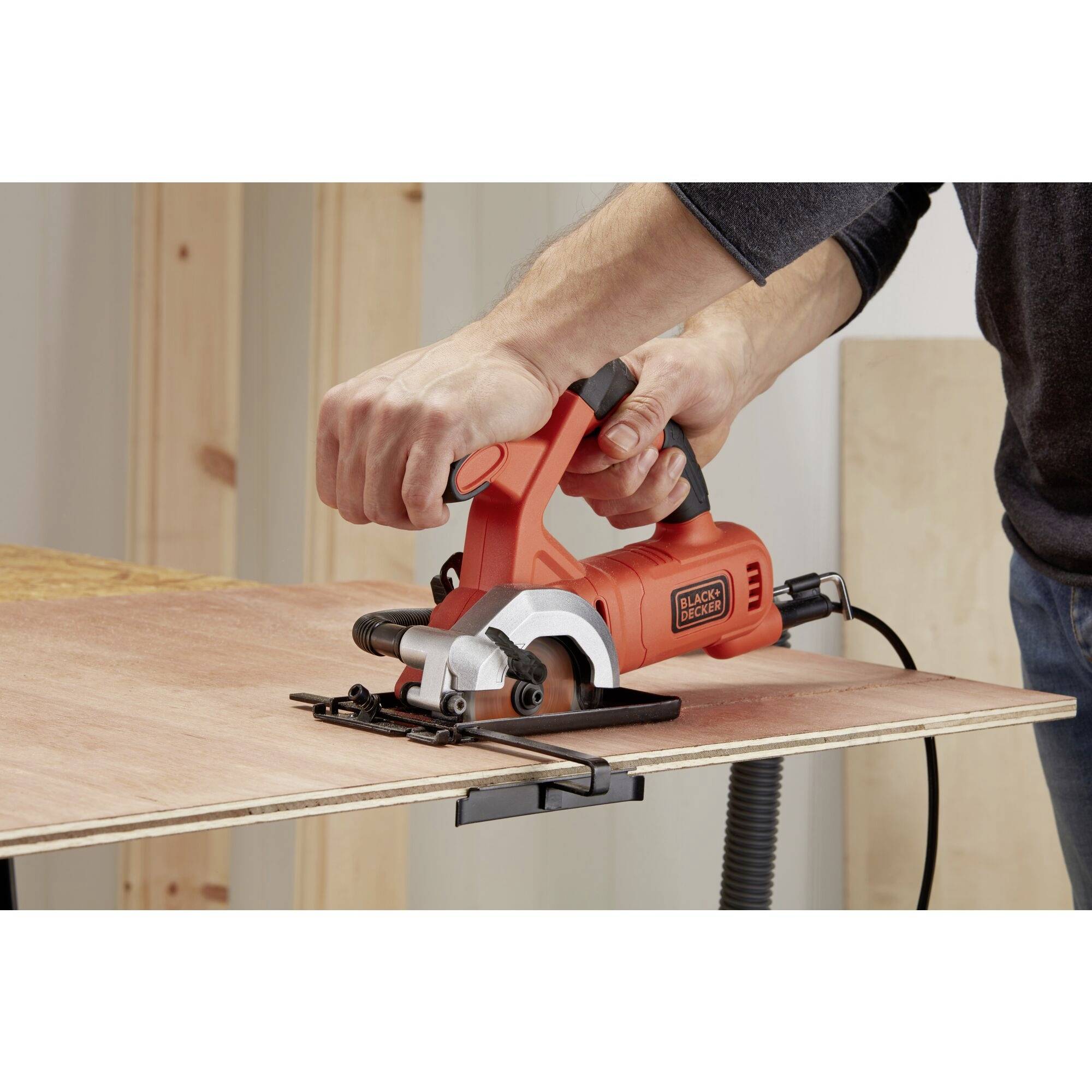 A person is using an electric handheld planer to smooth a wooden board. Device colour: orange. Environment: workshop.