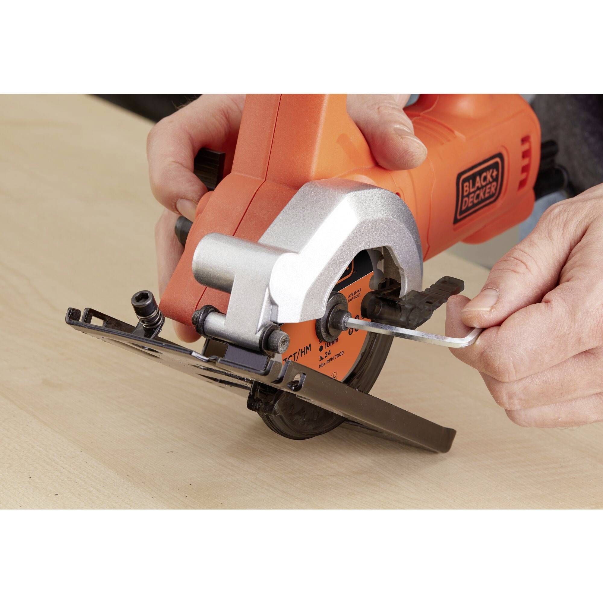 A person is using an orange electrical power tool attachment to install a circular saw blade on a table.