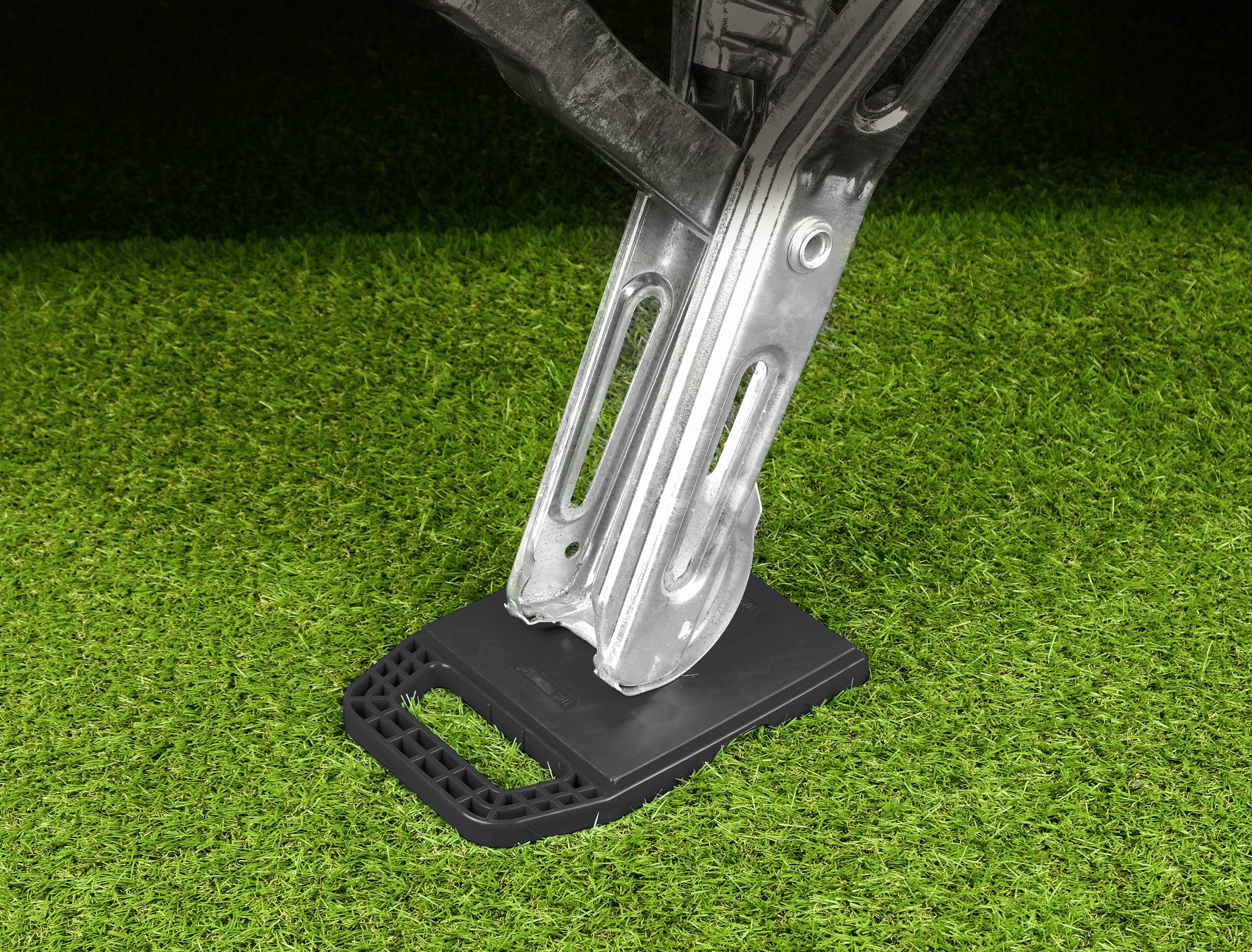 A jack lifts a vehicle on a patch of green grass. The jack is standing on a stable, black base.