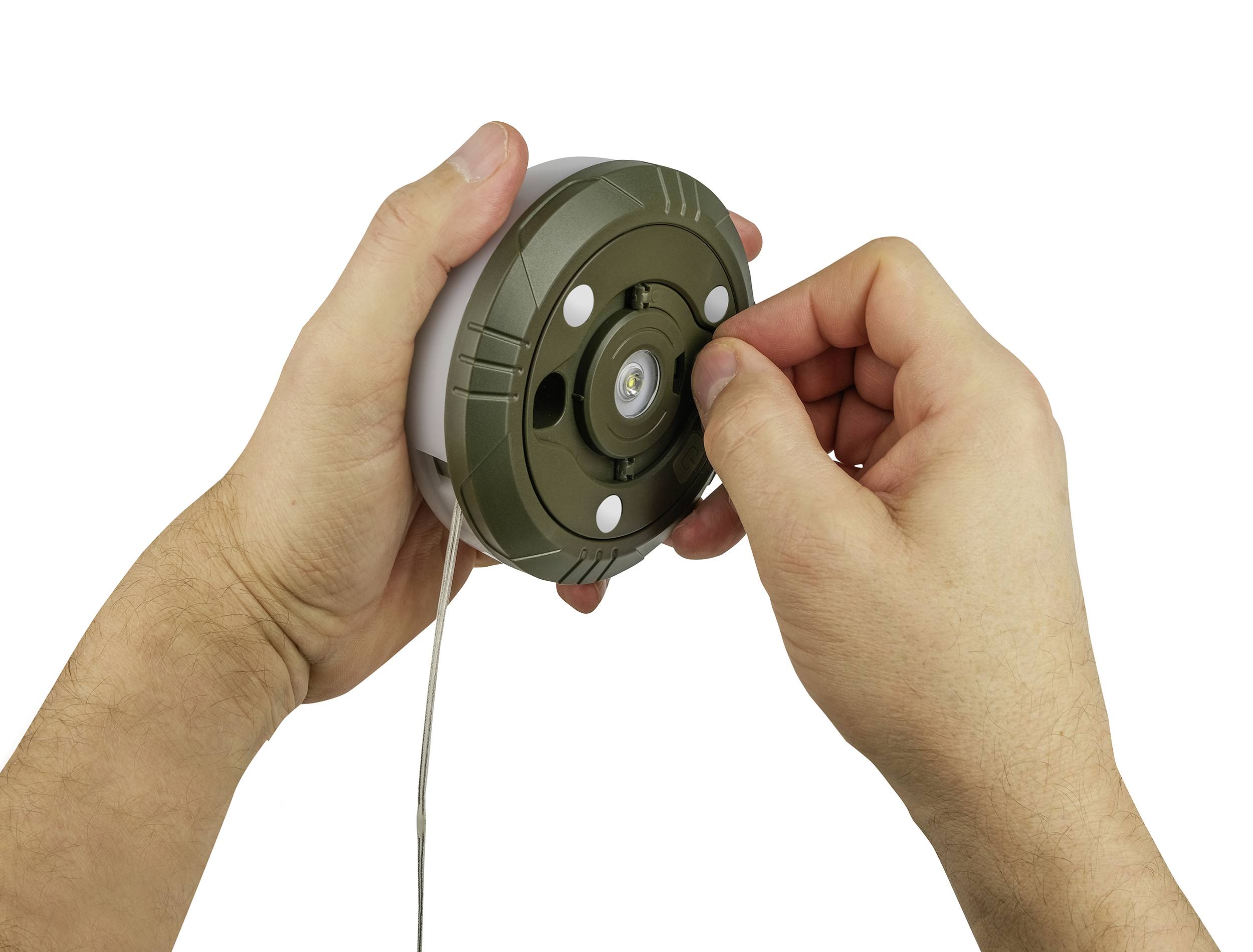 Two hands are holding a round, green object, while a finger adjusts a small component in the centre.