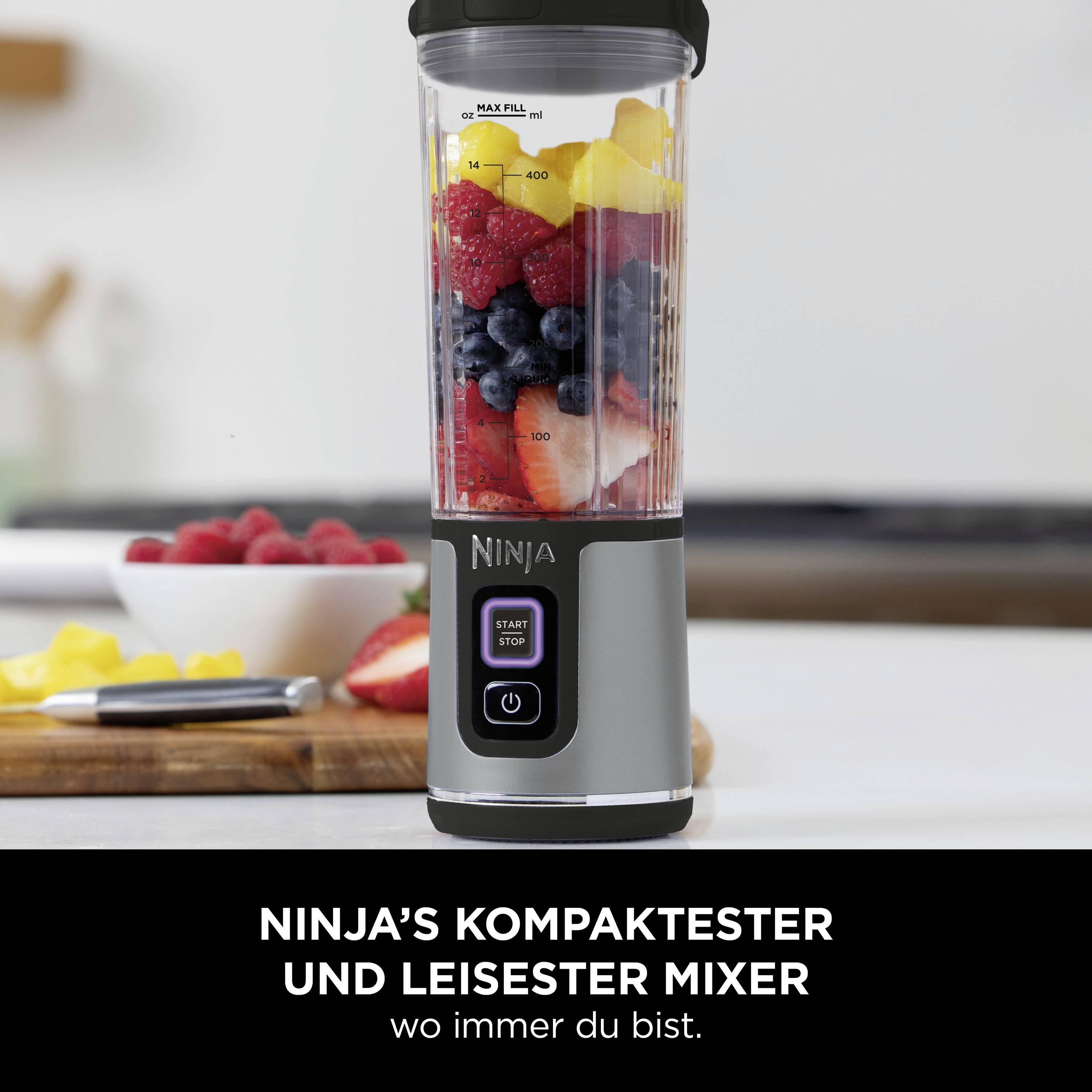 On a kitchen table stands a blender, filled with fruit such as bananas, berries and mango. Text below: 'Ninja's most compact and quietest blender wherever you are.'