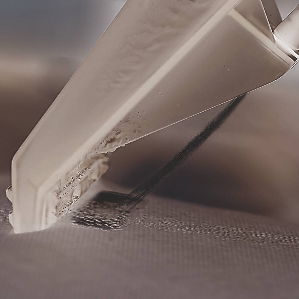 Close-up of a white plastering trowel being drawn across a smooth surface, removing a strip of dirt.