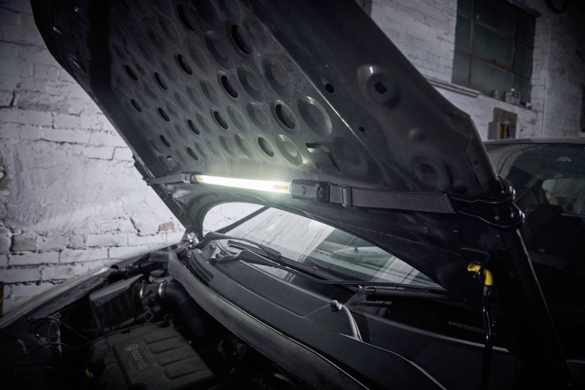 Car workshop: A bonnet is open and a lamp illuminates the engine bay of a vehicle to facilitate repairs.