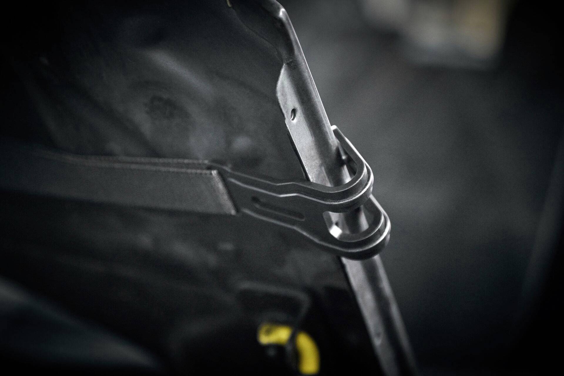 Close-up of a black metal hook holding a strap, presumably attached to a car door. The background is out of focus.