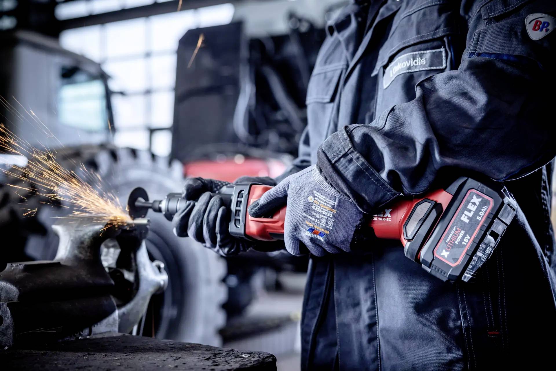 A person is working with an angle grinder, sparks flying. They are wearing protective clothing, with tools and machinery visible in the background.