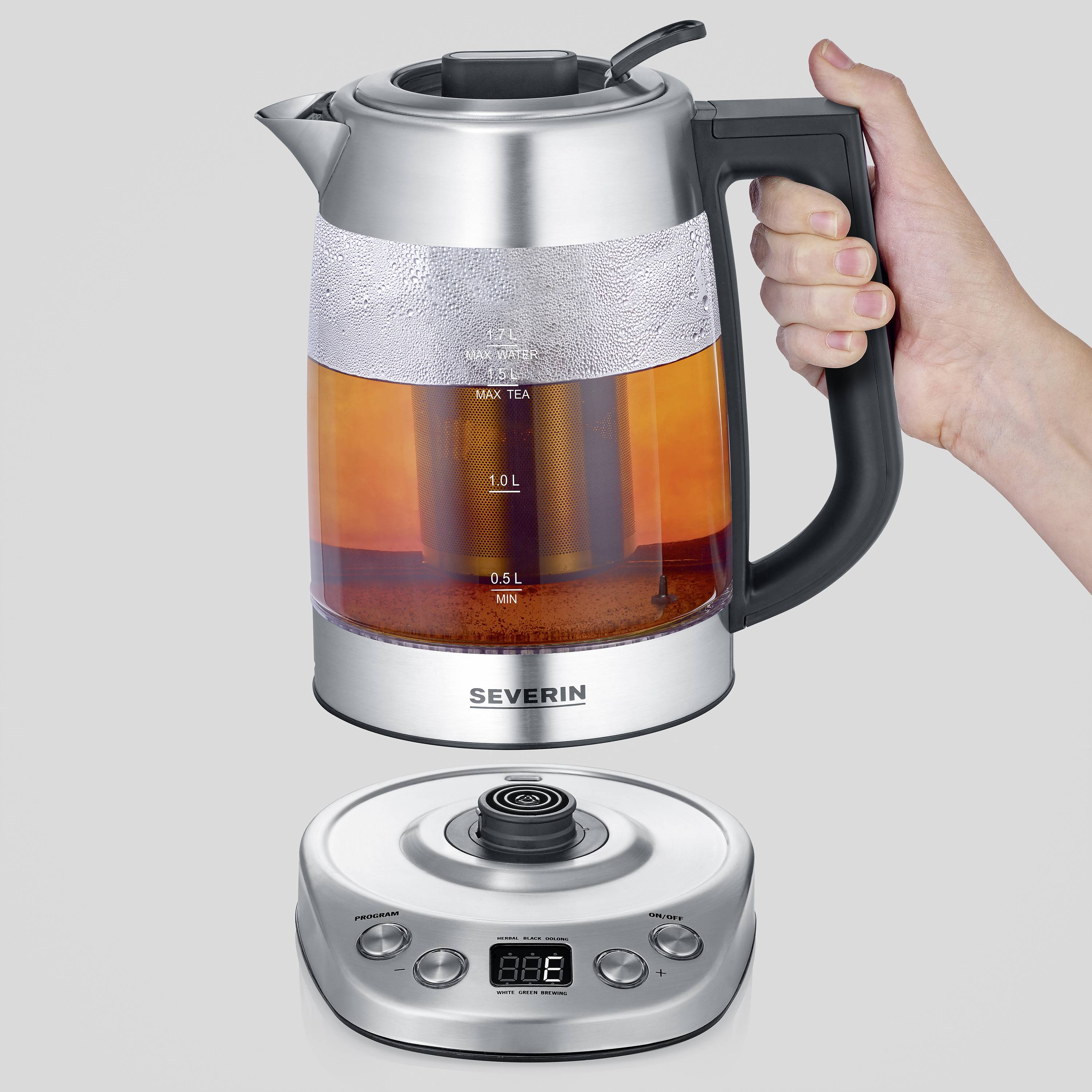 A hand is holding a transparent kettle with a black handle. The kettle is situated on a silver base with a digital display.