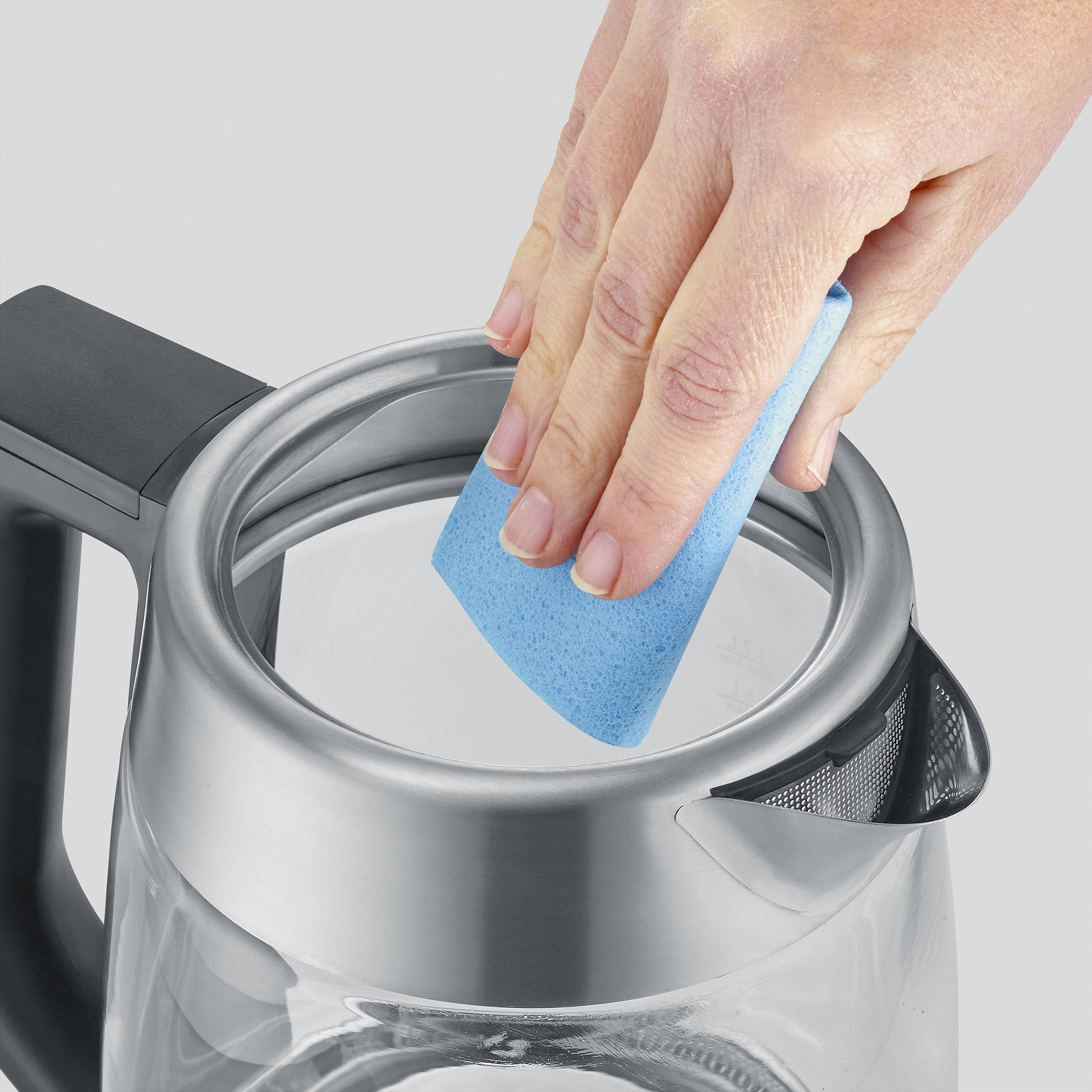 A hand is cleaning the inside of a kettle with a blue sponge.