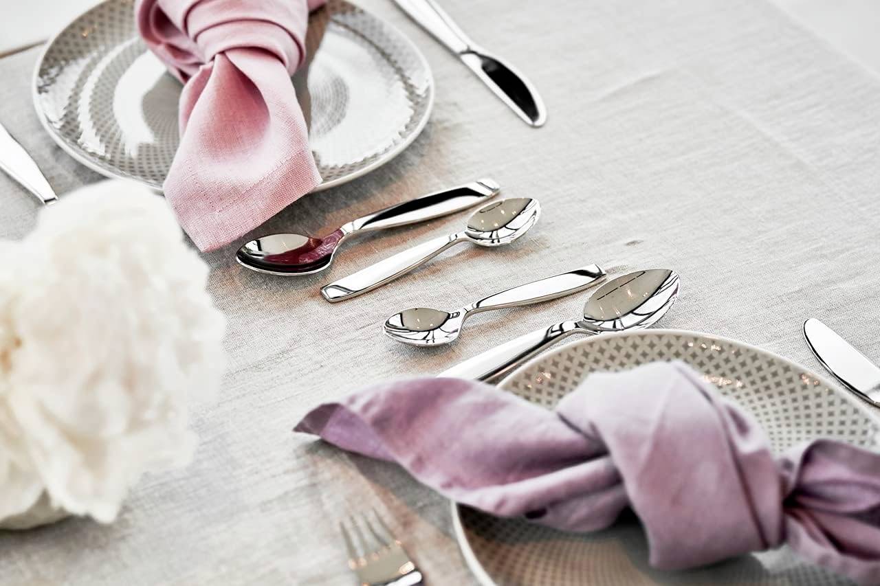 Elegant table setting with two plates, silver cutlery and pink fabric napkins tied in a knot on a light grey tablecloth.