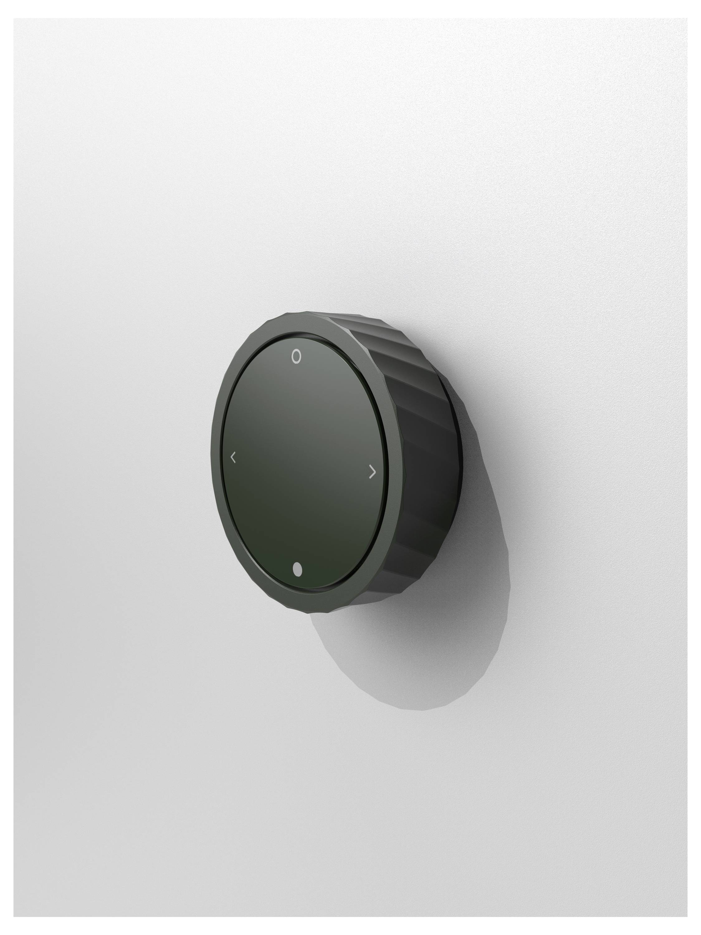 Black, round rotary dial on a white wall, with arrows indicating four directions, likely for volume control.